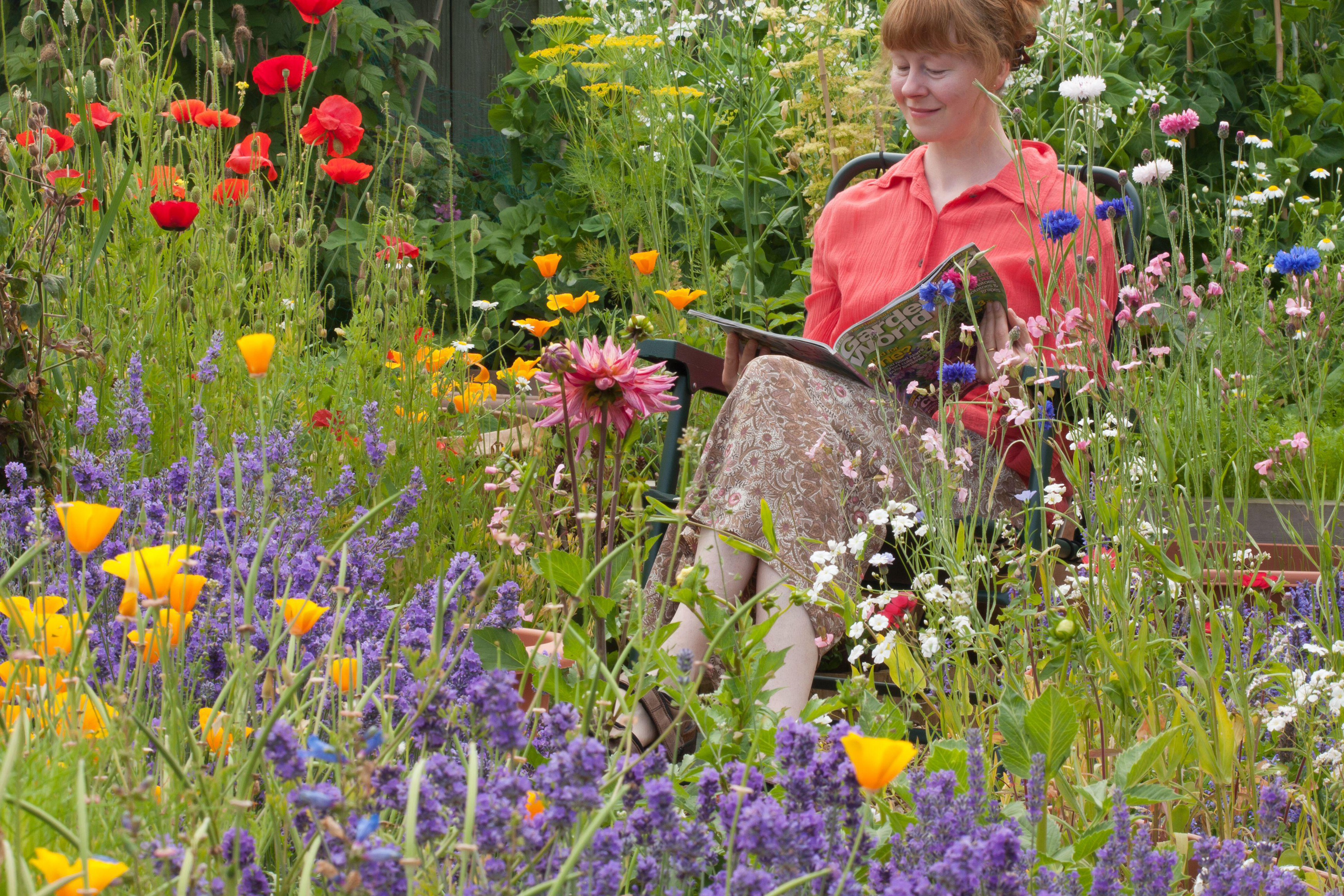 Woman sitting in a garden surrounded by colourful plants (Alamy/PA)