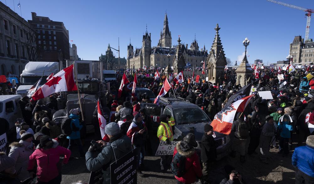 Protestors mingle around vehicles parked on Wellington St. in front of West Block and the Parliament buildings as they participate in a cross-country truck convoy protesting measures taken by authorities to curb the spread of COVID-19 and vaccine mandates in Ottawa on Saturday,.