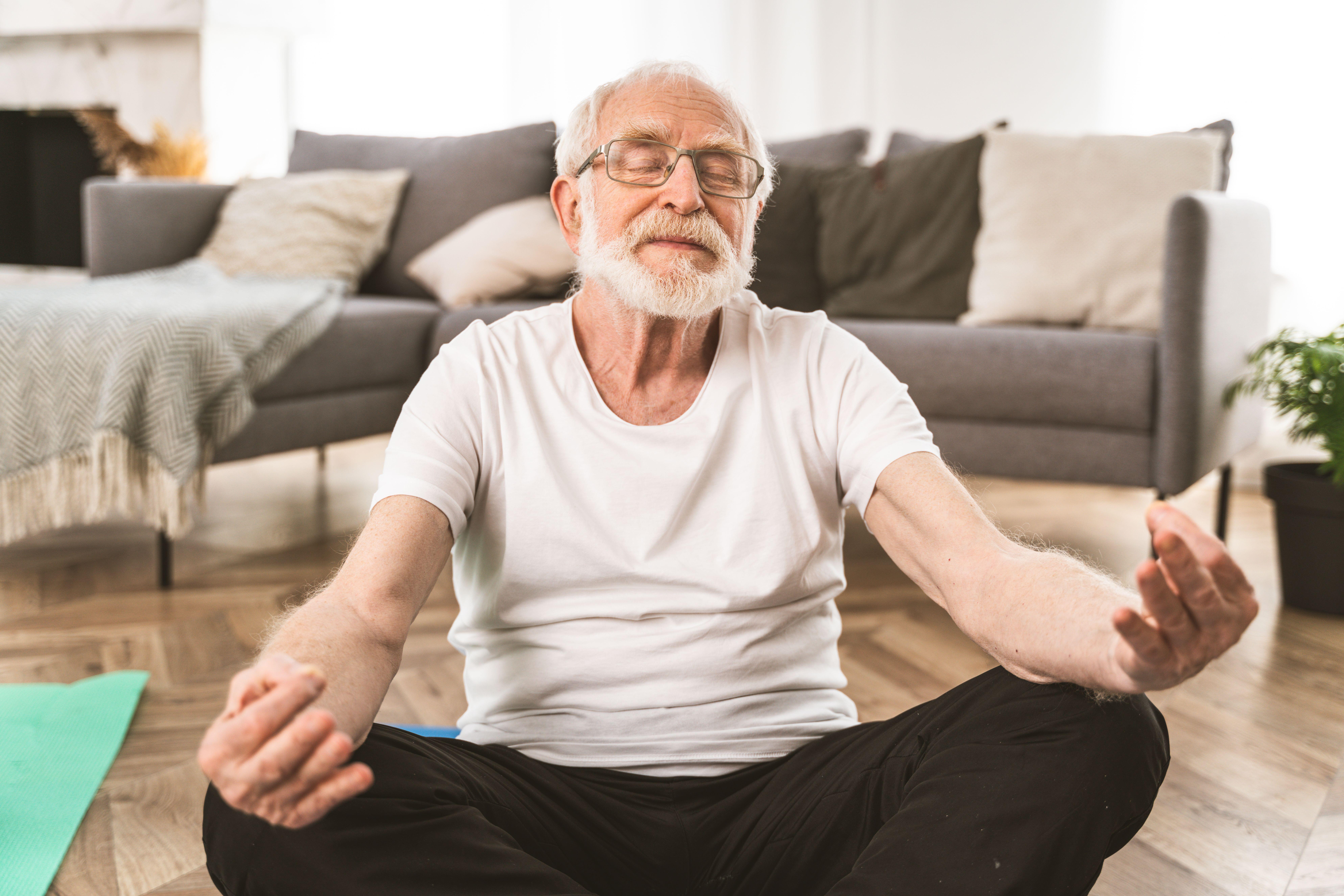 Mature man sitting on living room floor doing meditation