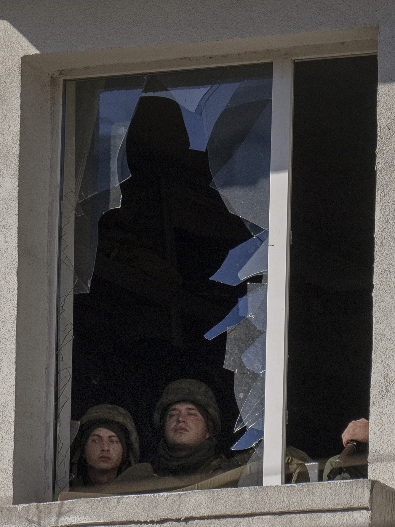 Ukrainian soldiers look out from a broken window inside a military facility