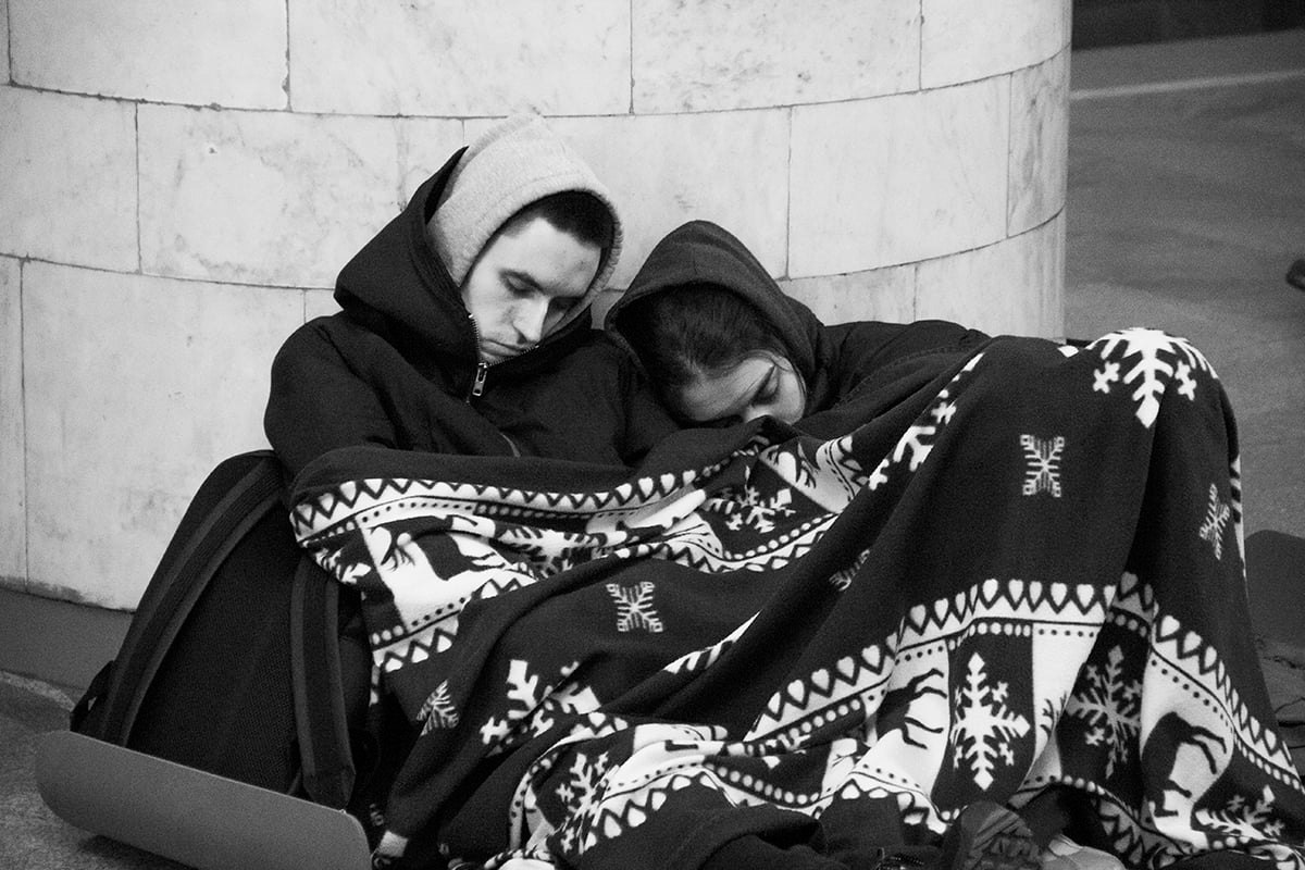 Civilian's are see huddled together under a blanket and wearing layers of clothing. 