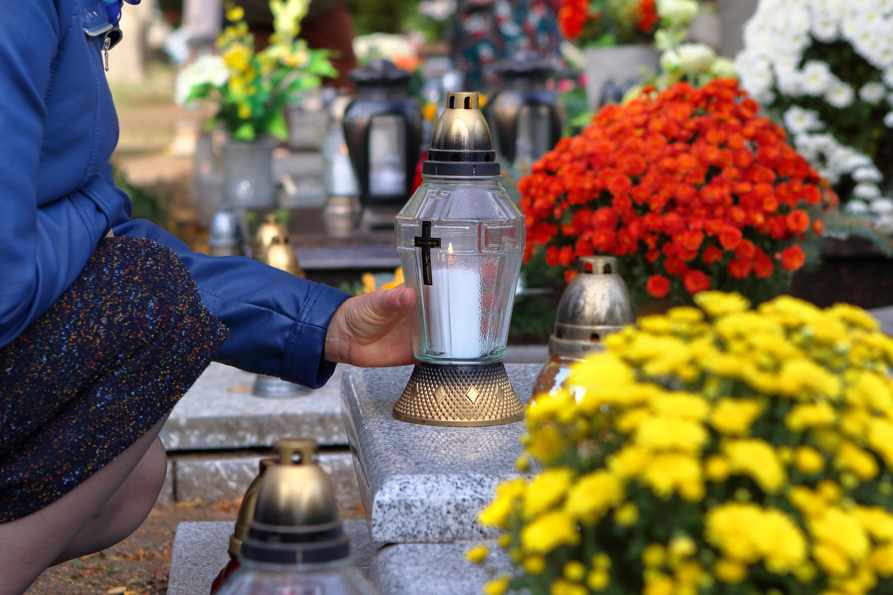 Woman at the cemetery puts a candle on a grave