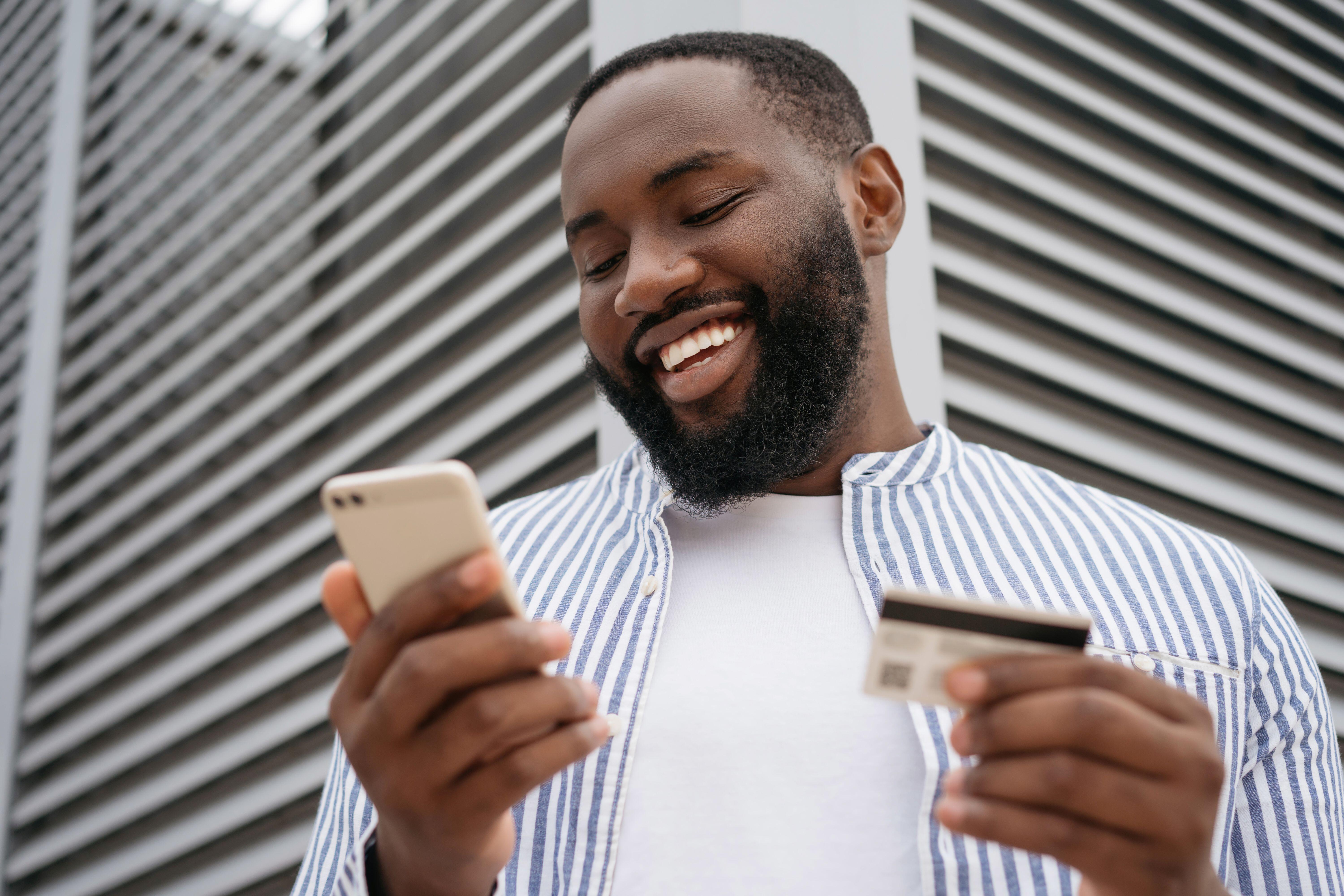 Man looking at his phone smiling with a credit card