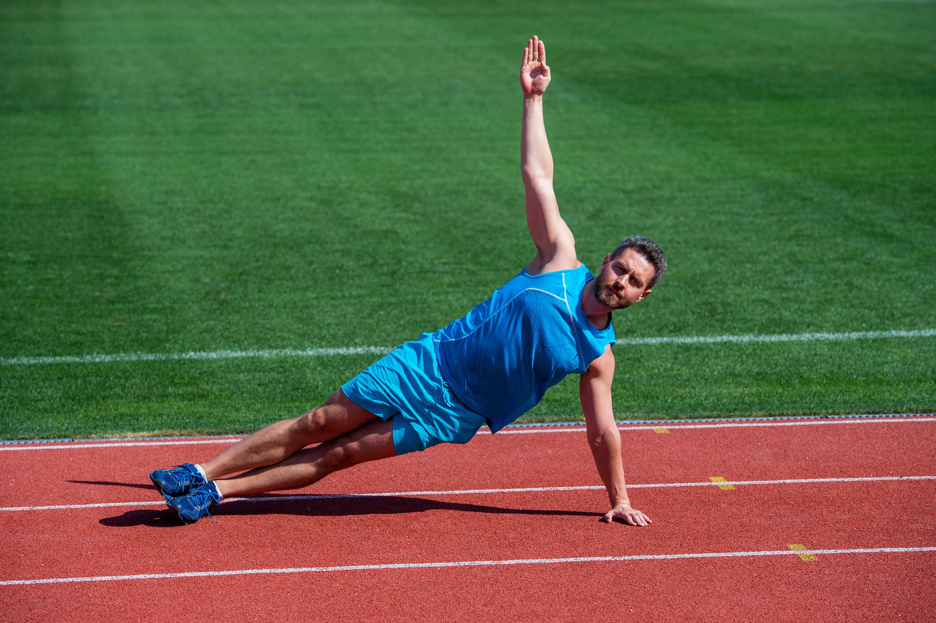 Man doing side plank on athletics track in sun