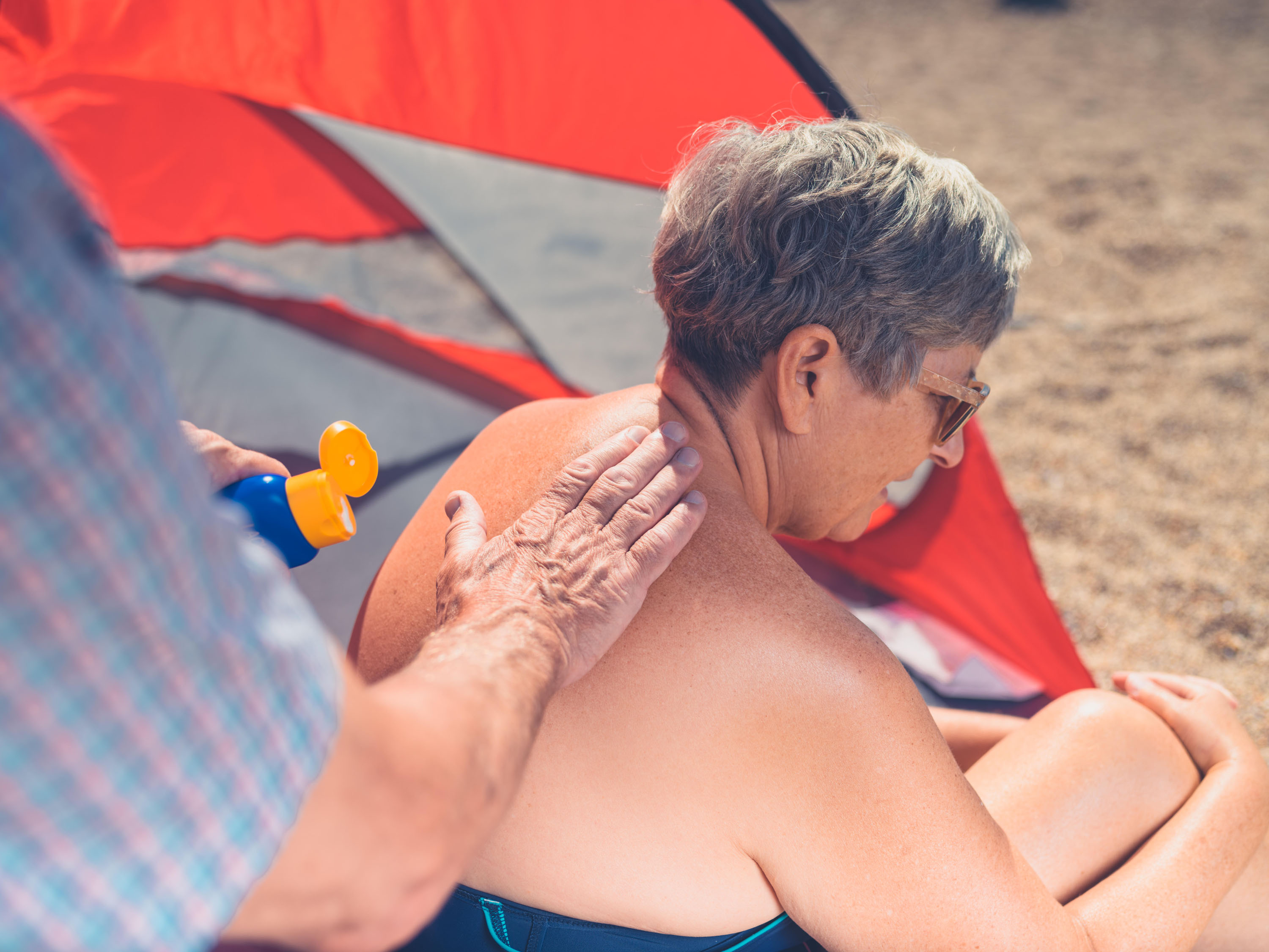Woman having sun cream applied to her back at the beach.