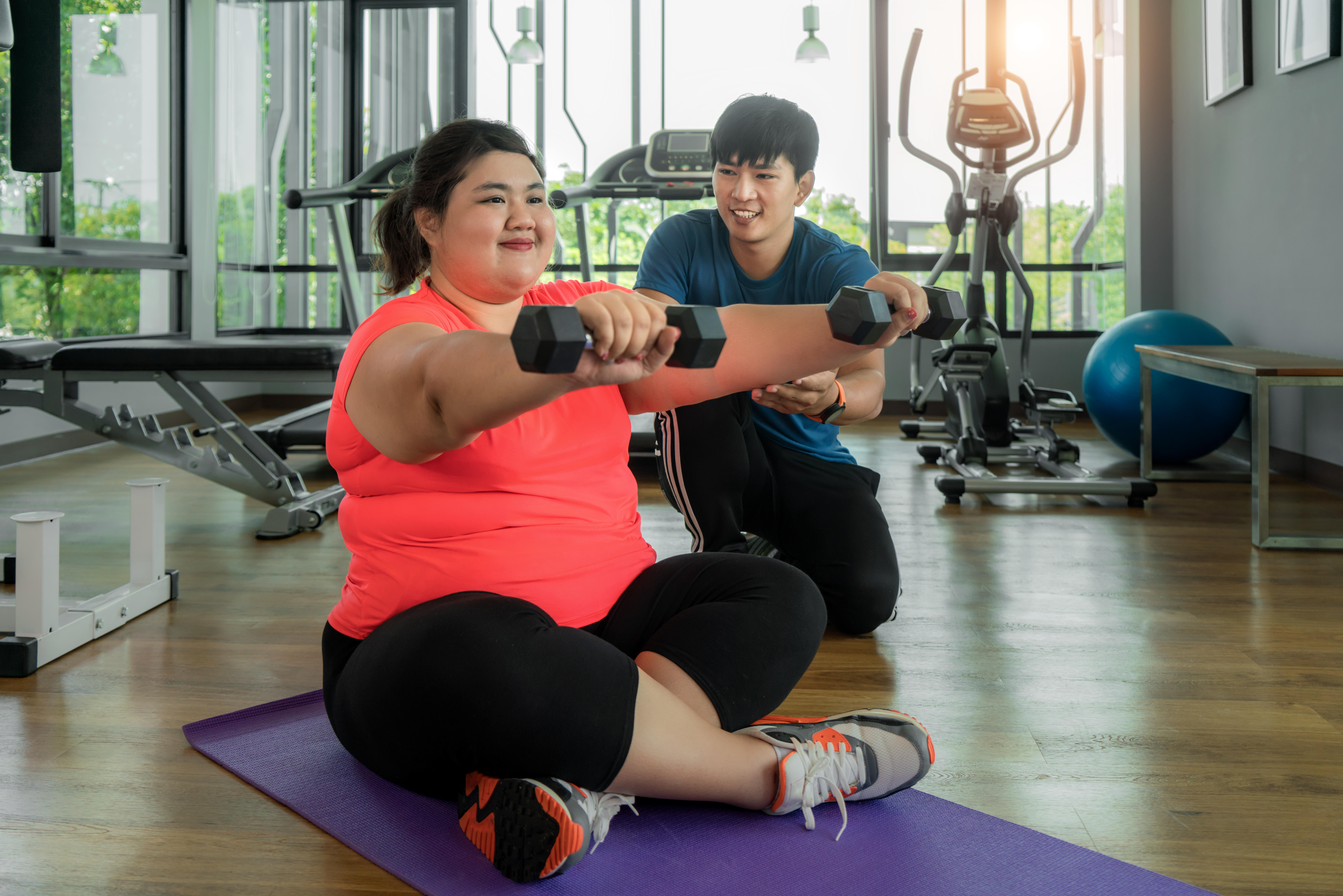 Woman using dumbbells in the gym with her trainer