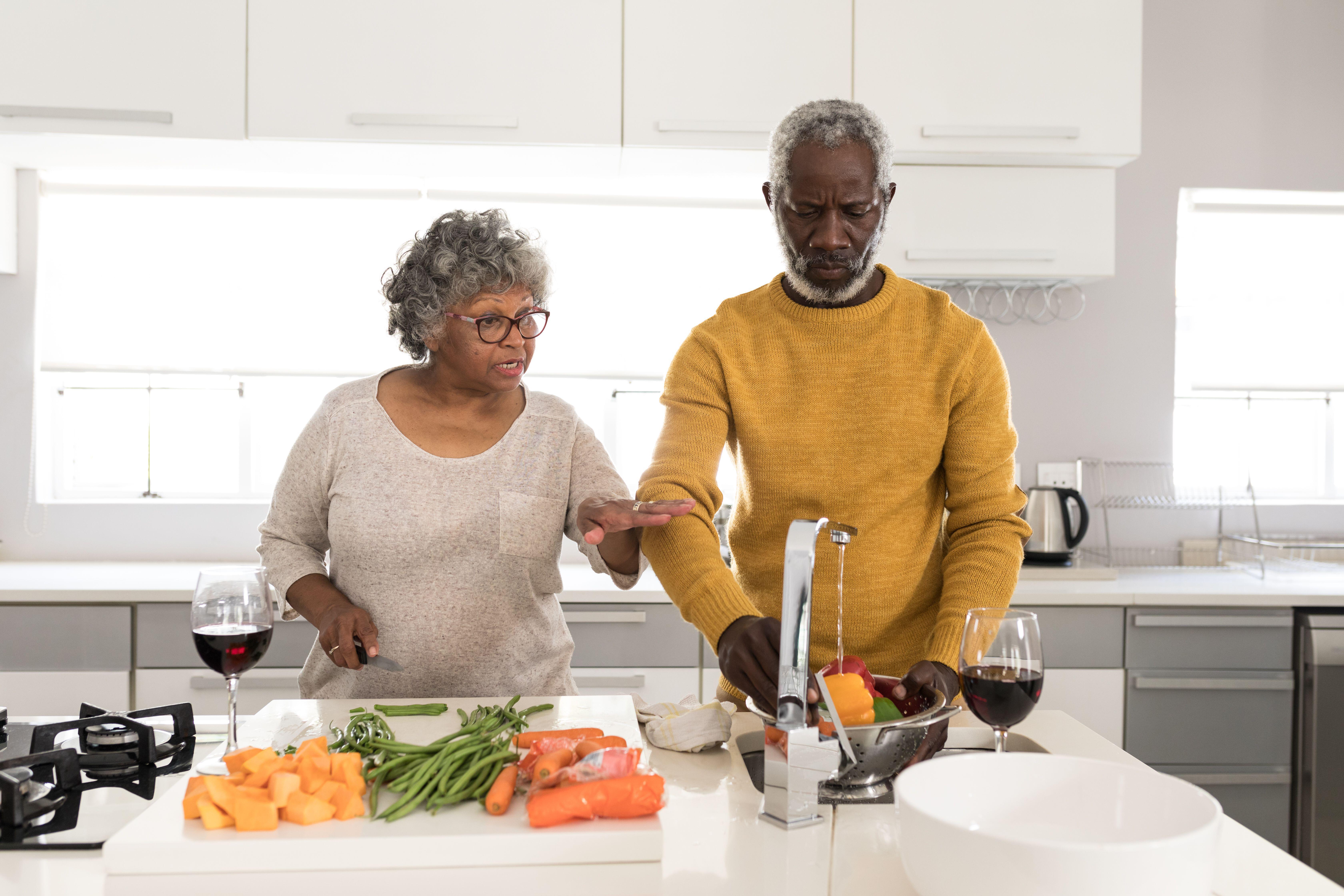 Black couple preparing food in the kitchen, washing veg and chatting