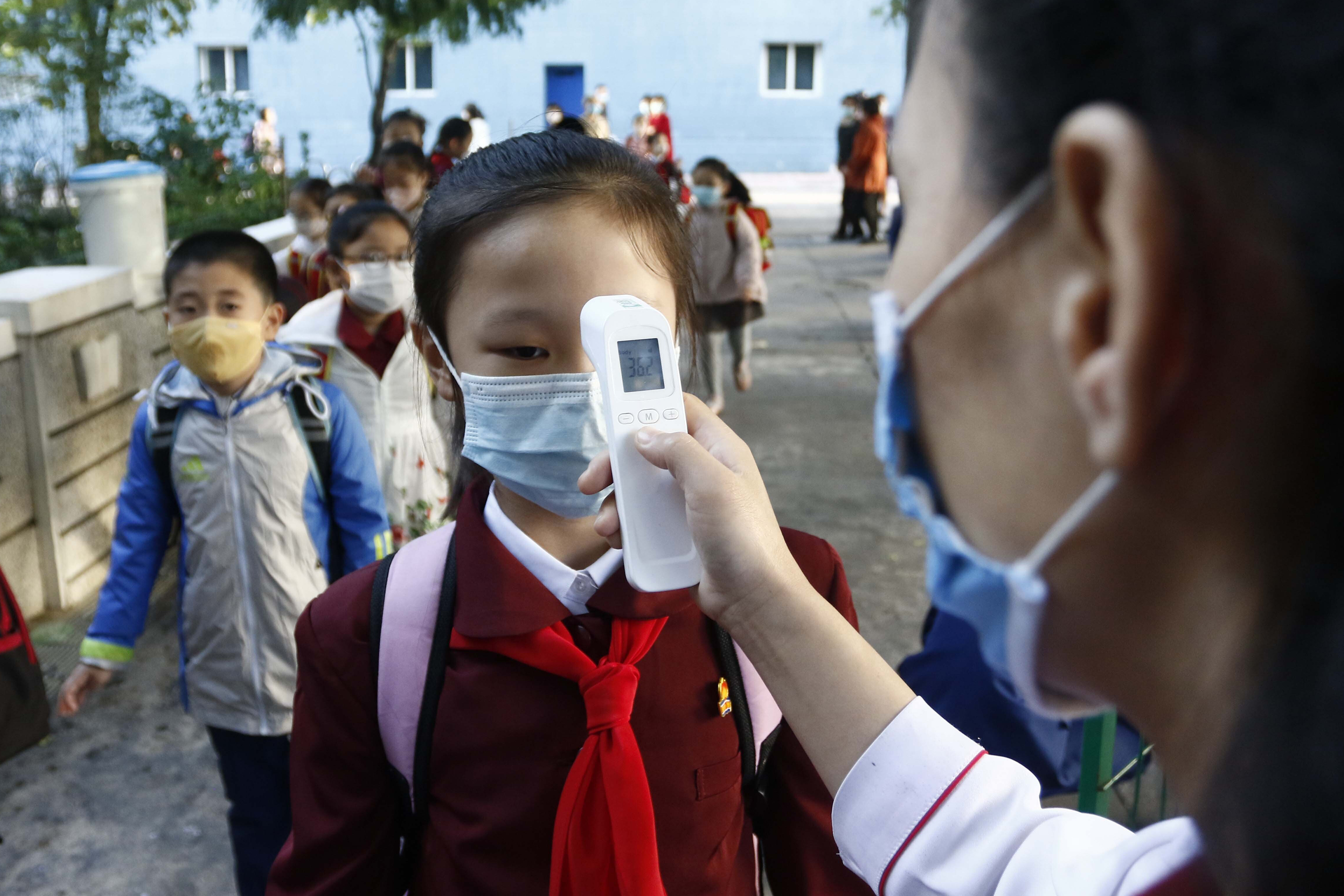 A teacher takes the body temperature of a schoolgirl to help curb the spread of the coronavirus before entering Kim Song Ju Primary School in Central District in Pyongyang, North Korea, Wednesday, Oct. 13, 2021