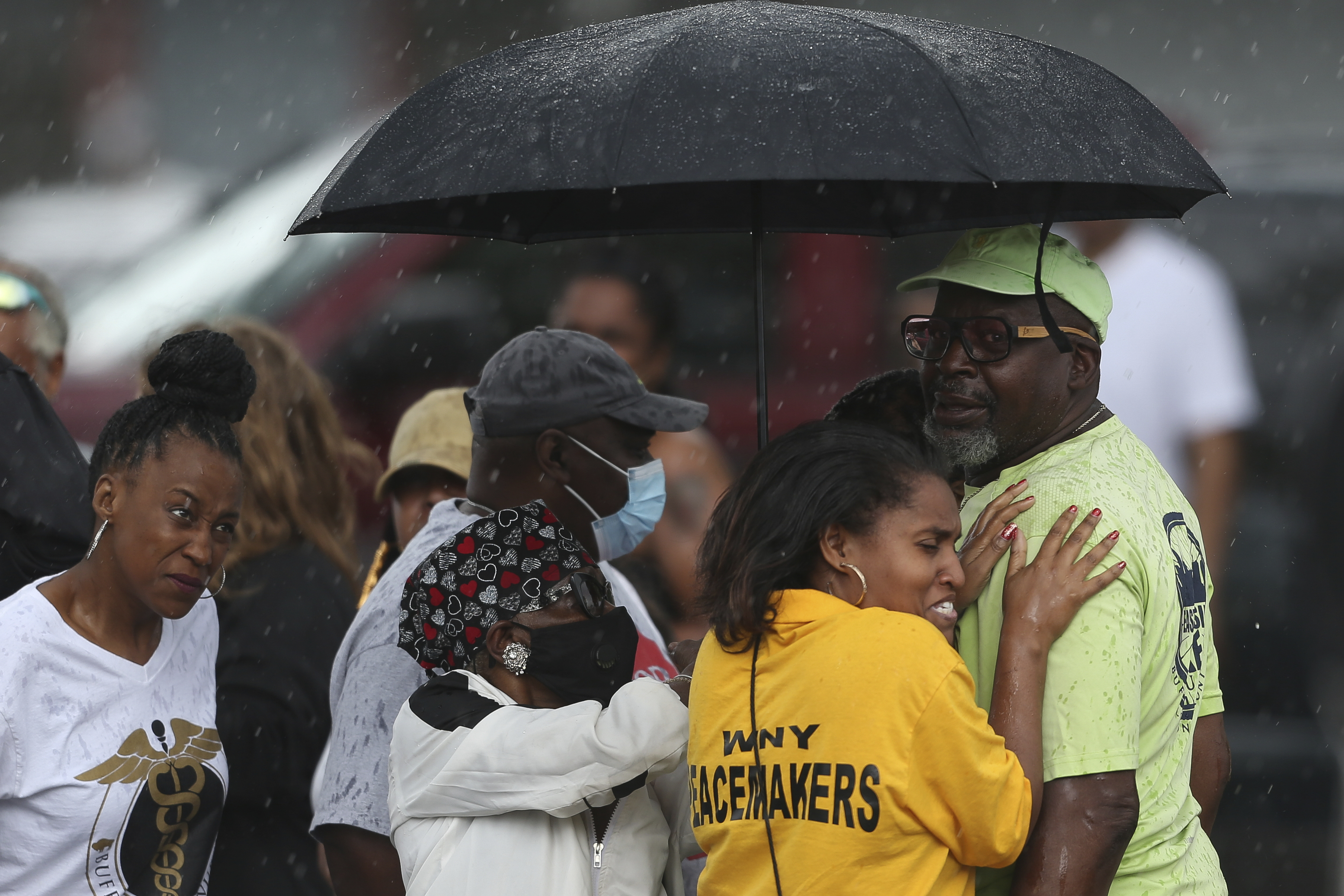 Bystanders gather under an umbrella as rain rolls in after a shooting at a supermarket on Saturday, May 14, 2022, in Buffalo
