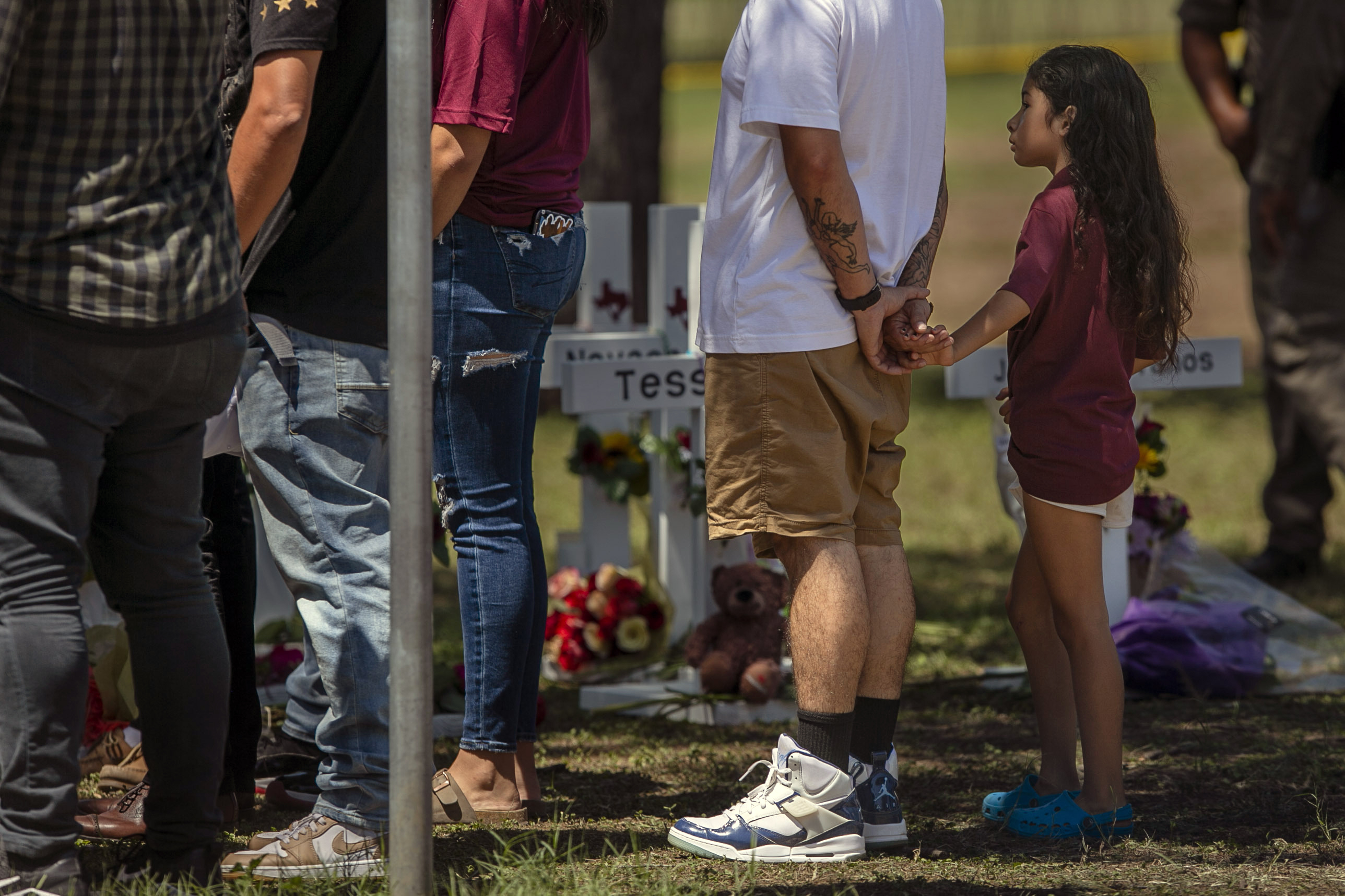 A young person holds onto an adults hand as they visit the memorial created outside Robb Elementary School in Uvalde, Texas, on Thursday