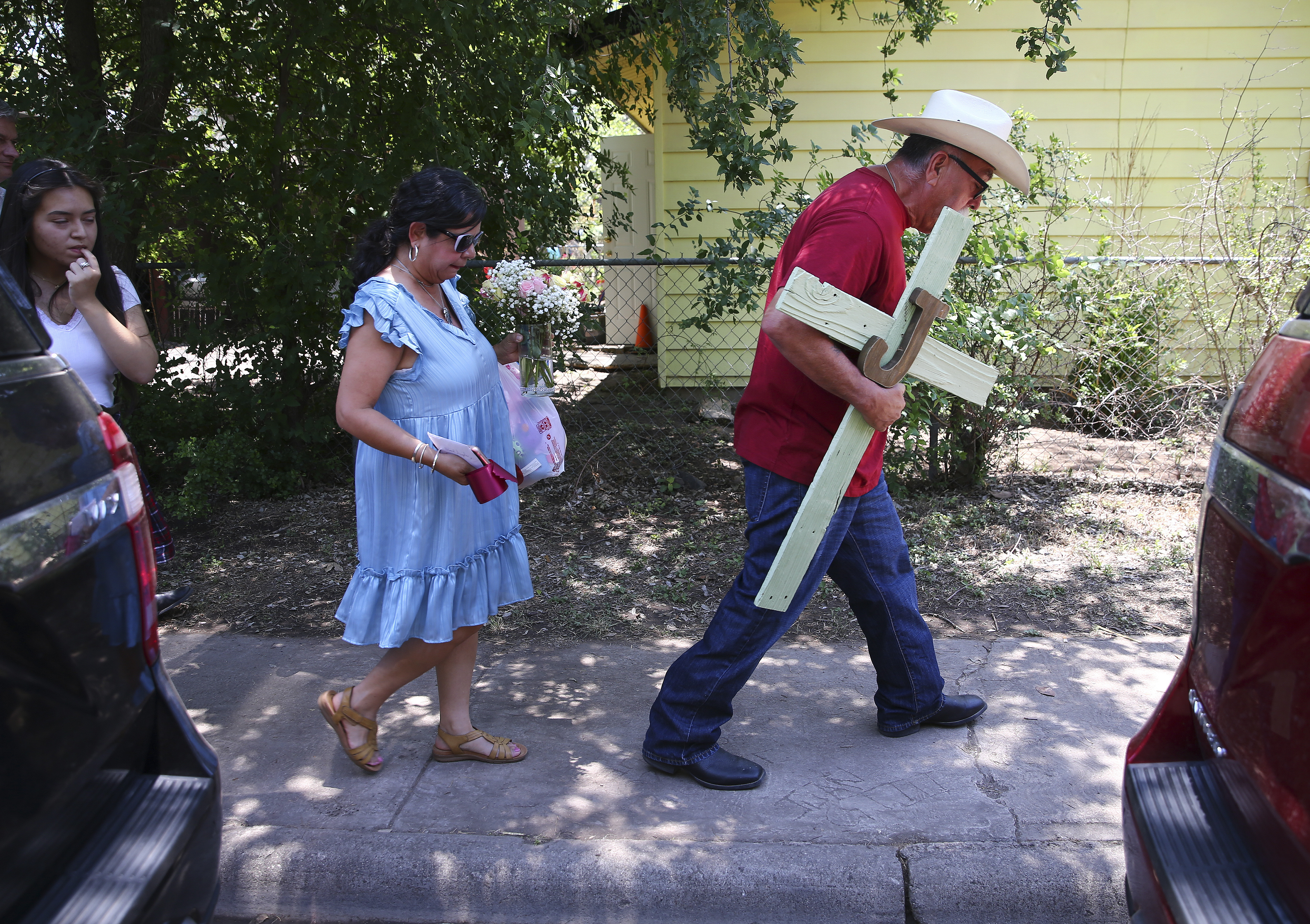 A man carries a cross he made as his wife, carries flowers to pay their respects to the 21 victims of the Robb Elementary School shooting in Uvalde, Texas on Thursday, May 26, 2022