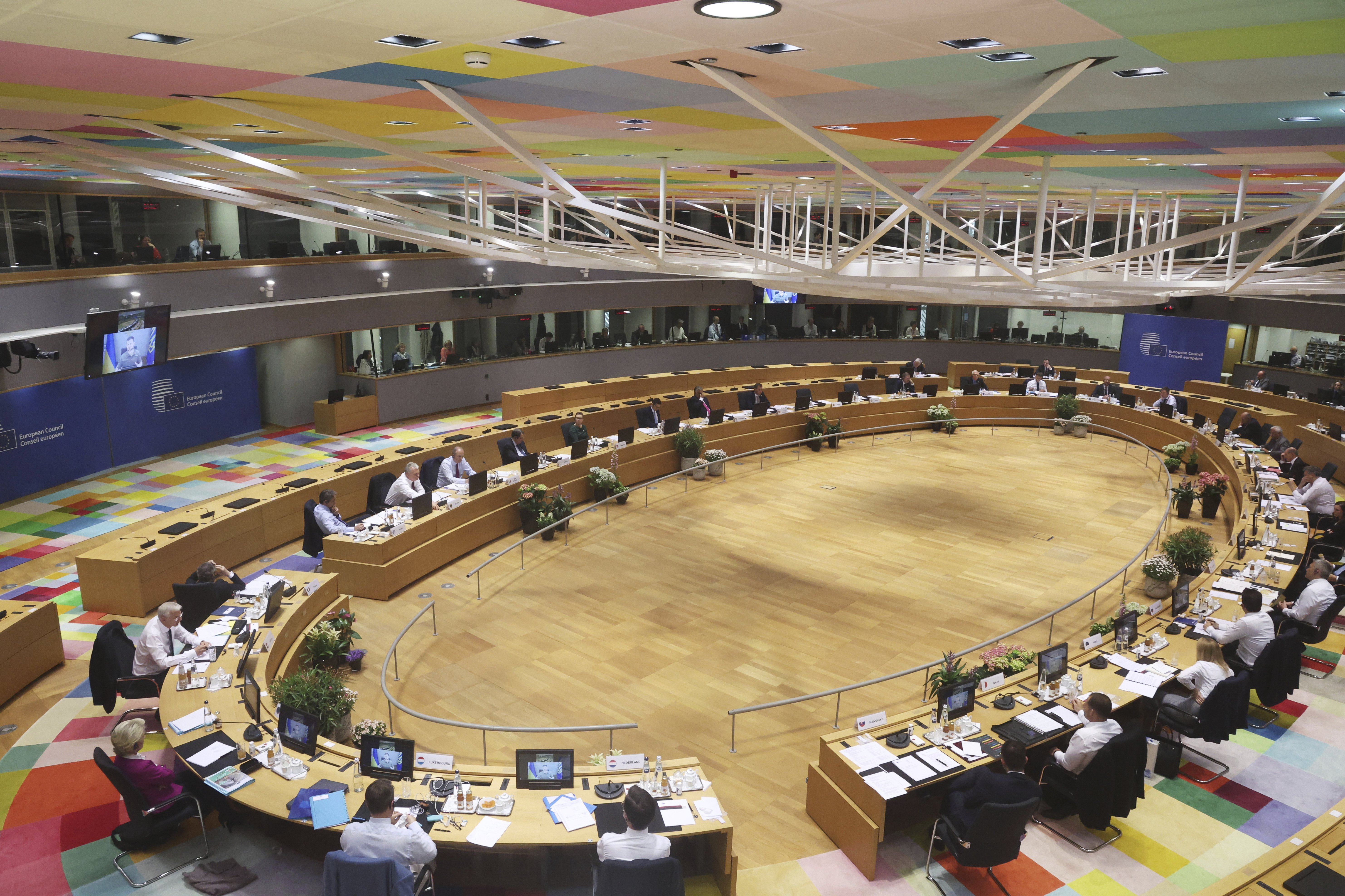 Ukrainian President Volodymyr Zelenskyy is seen on a screen, left, as addresses from Kyiv during an extraordinary meeting of EU leaders to discuss Ukraine, energy and food security at the Europa building in Brussels, on Monday