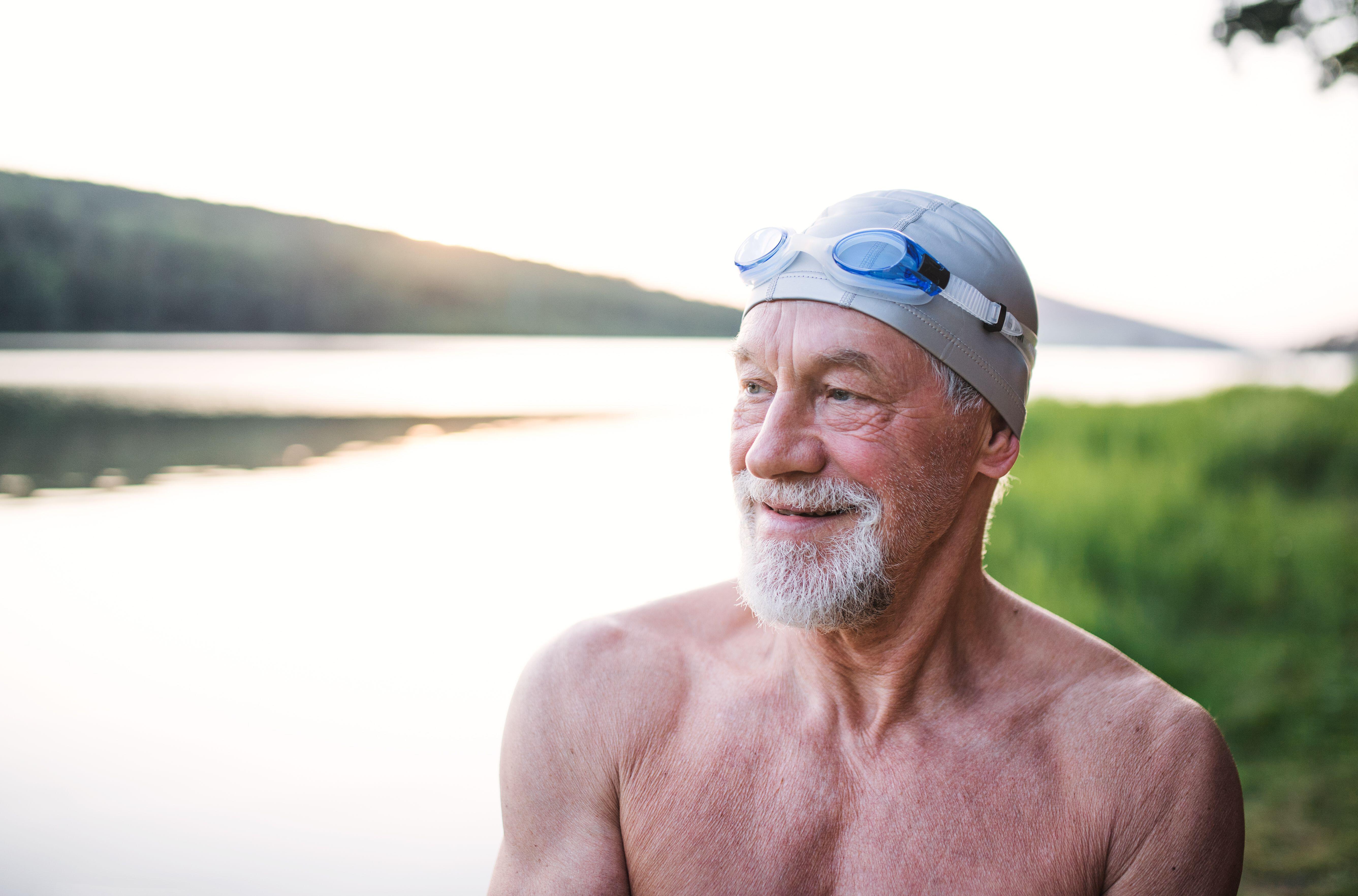 Mature man next to a lake, wearing swimming cap and goggles