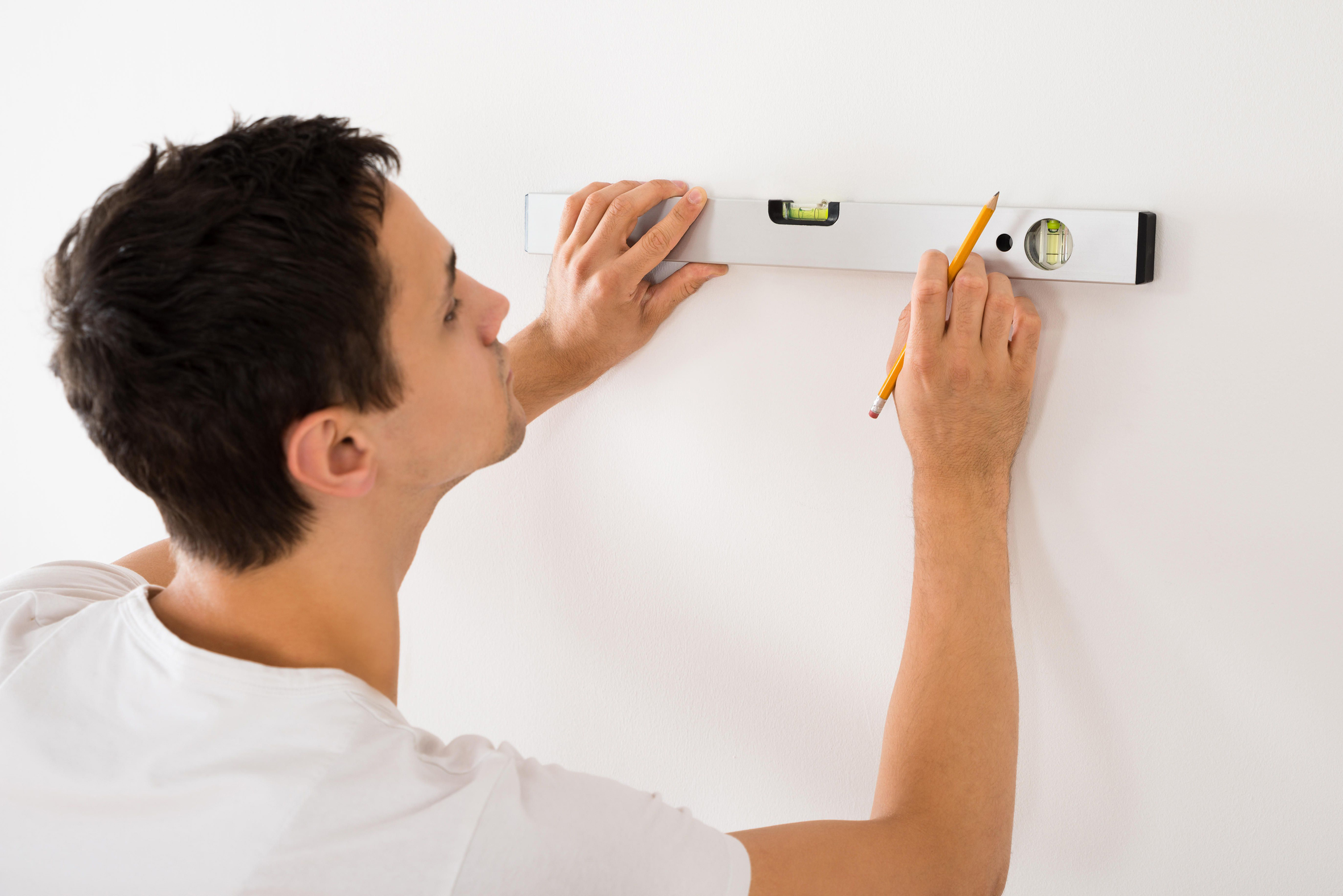 Man using a spirit level on white wall