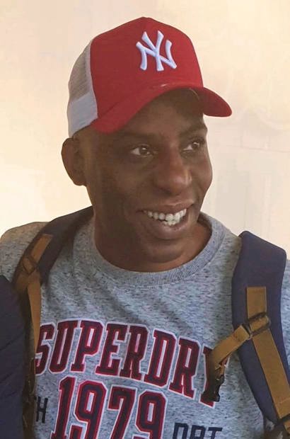 A picture of Oladeji Adeyemi Omishore, smiling and wearing a red baseball cap and grey t-shirt.