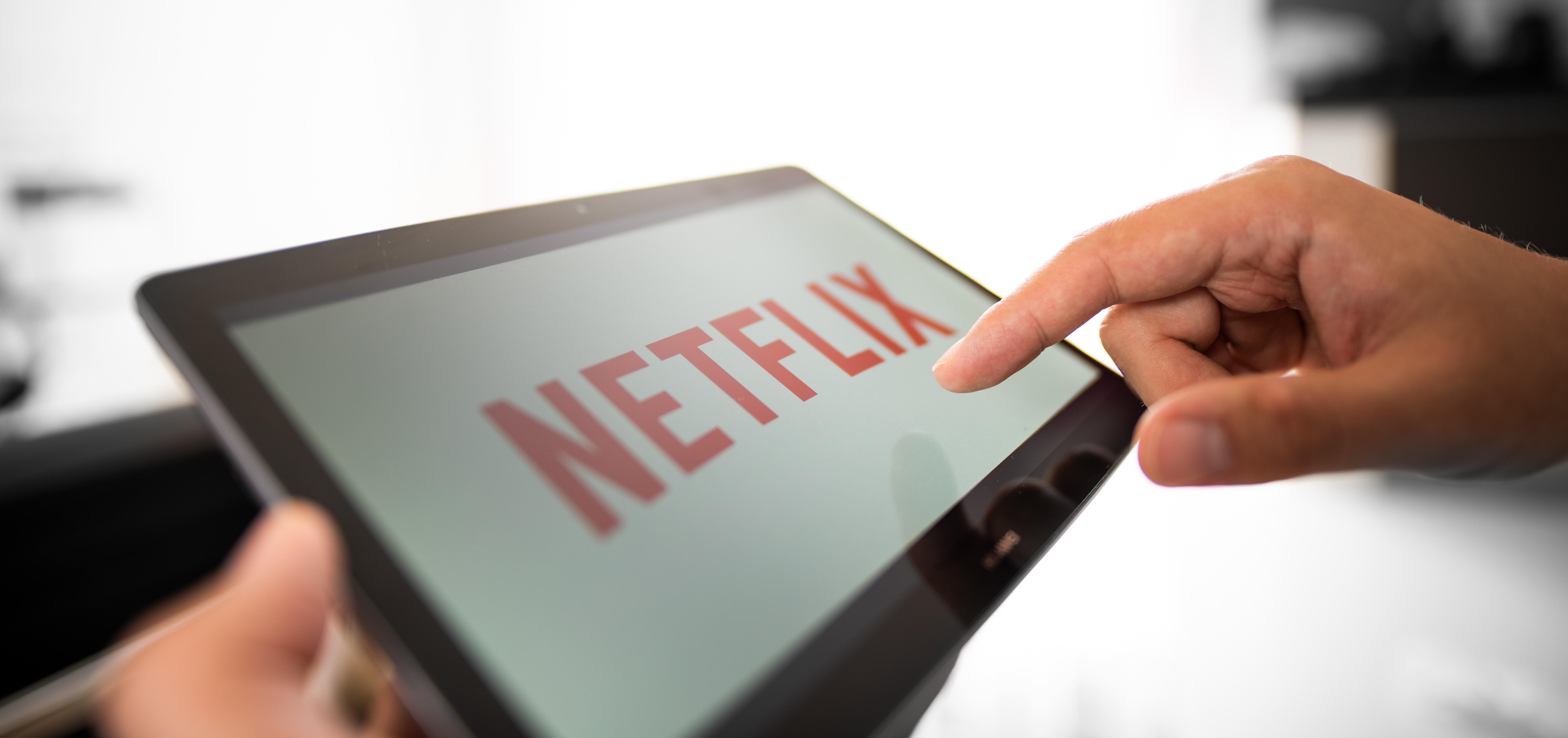 Hand reaches toward Netflix logo on screen