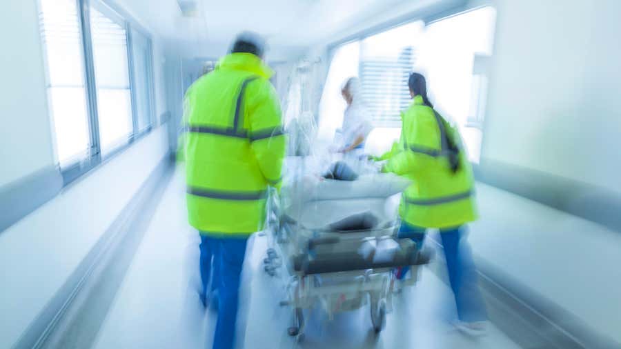 Motion blurred photograph of child patient on stretcher or gurney pushed at speed through hospital corridor by doctors and nurses