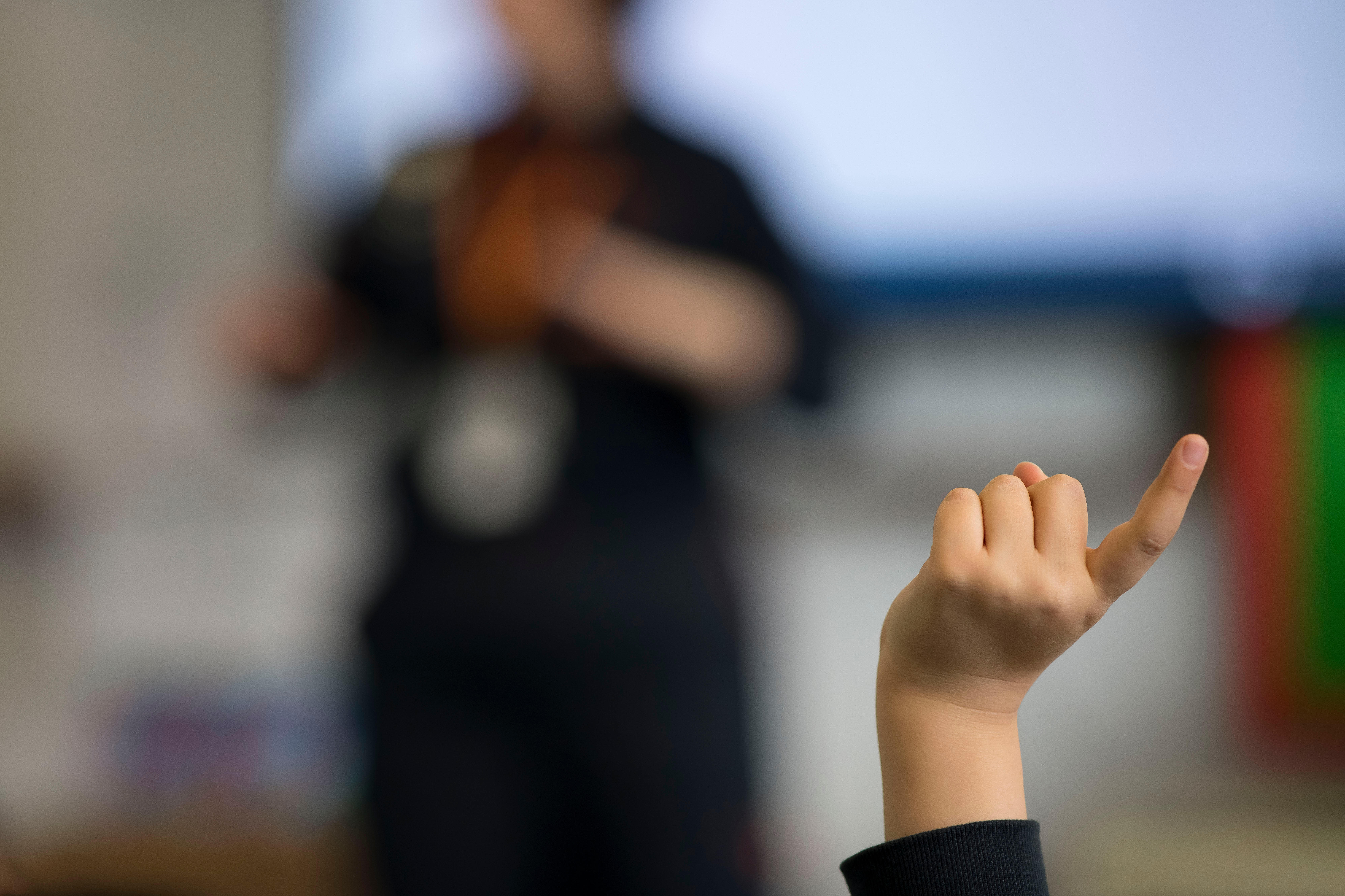 A young child puts his hand up when asked a question in a school classroom in Wales, UK