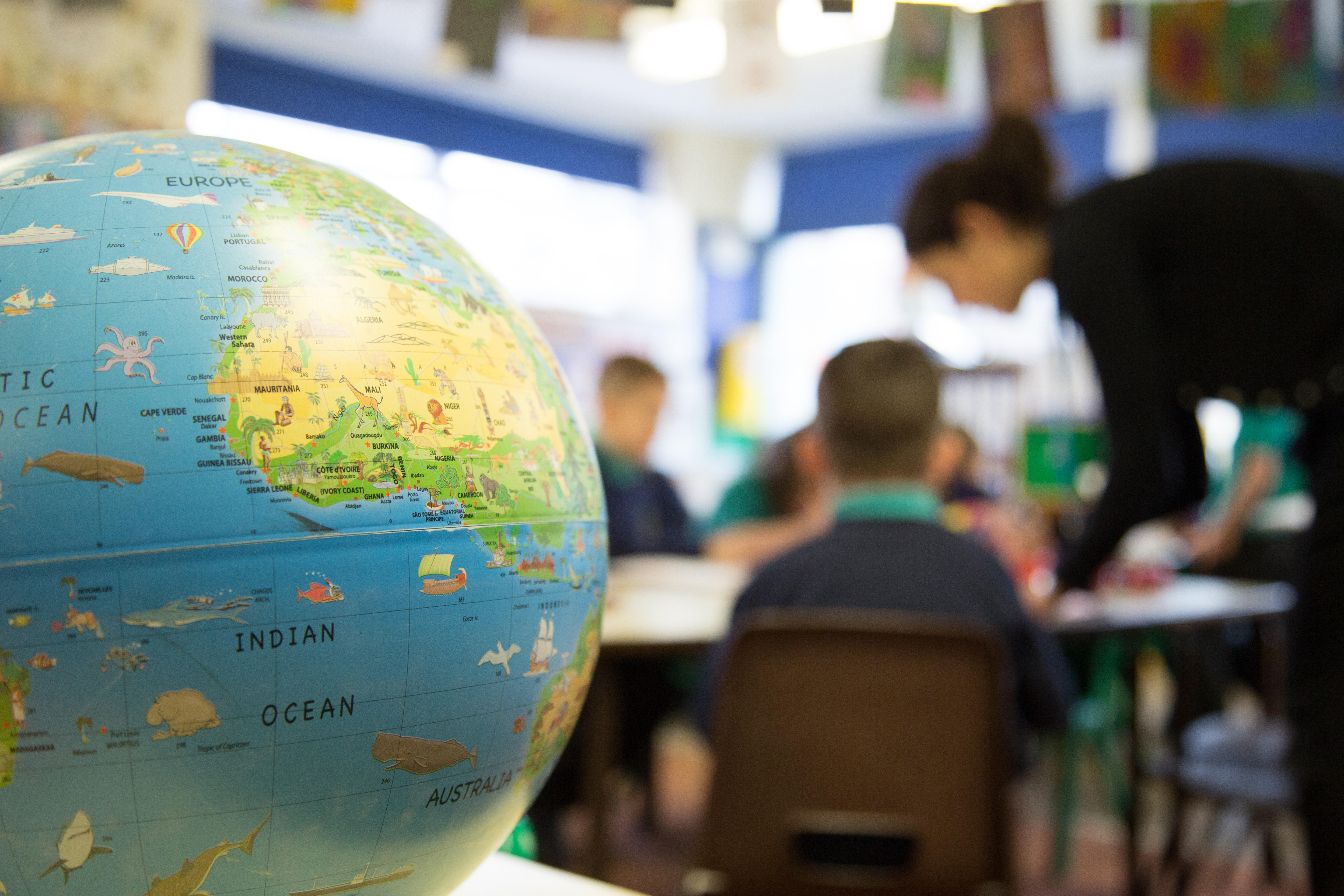 Teacher in a UK primary school classroom with a globe in the foreground