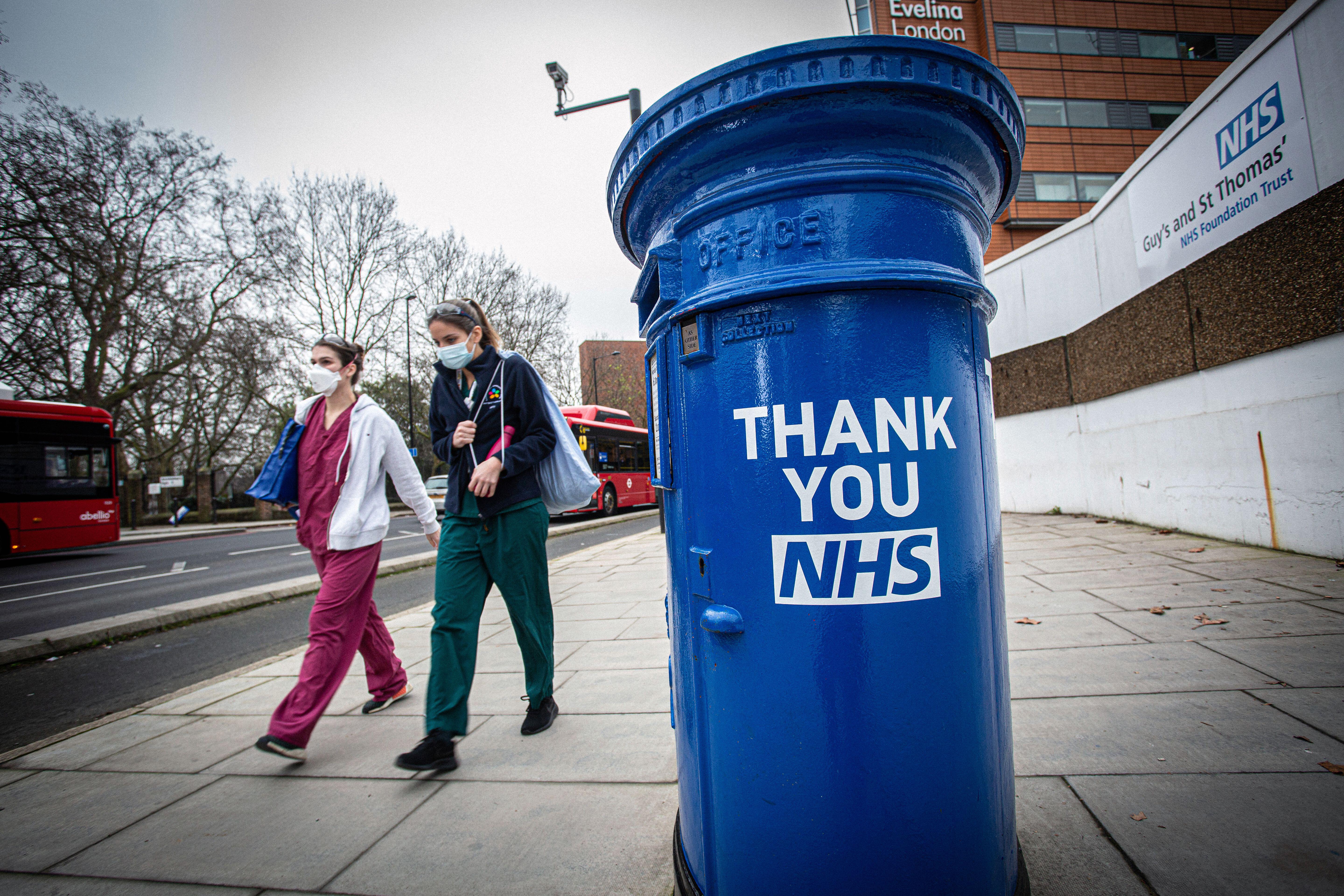 Nurses wearing a face masks walks past post box painted blue and carrying the message 'Thank You NHS' stands outside St Thomas' Hospital in London, UK