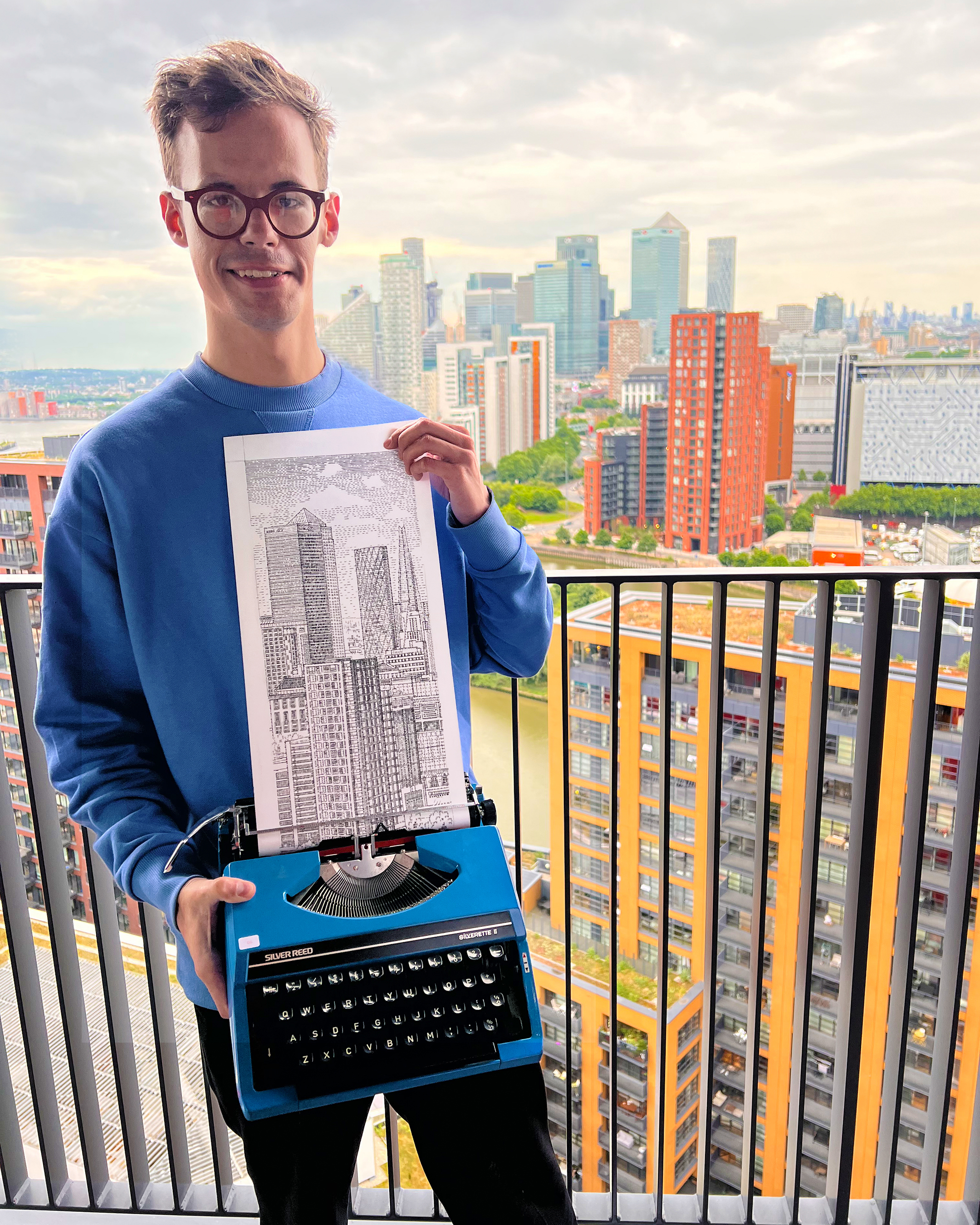 Man wearing a blue hoodie and holding a piece of art made using a typewriter