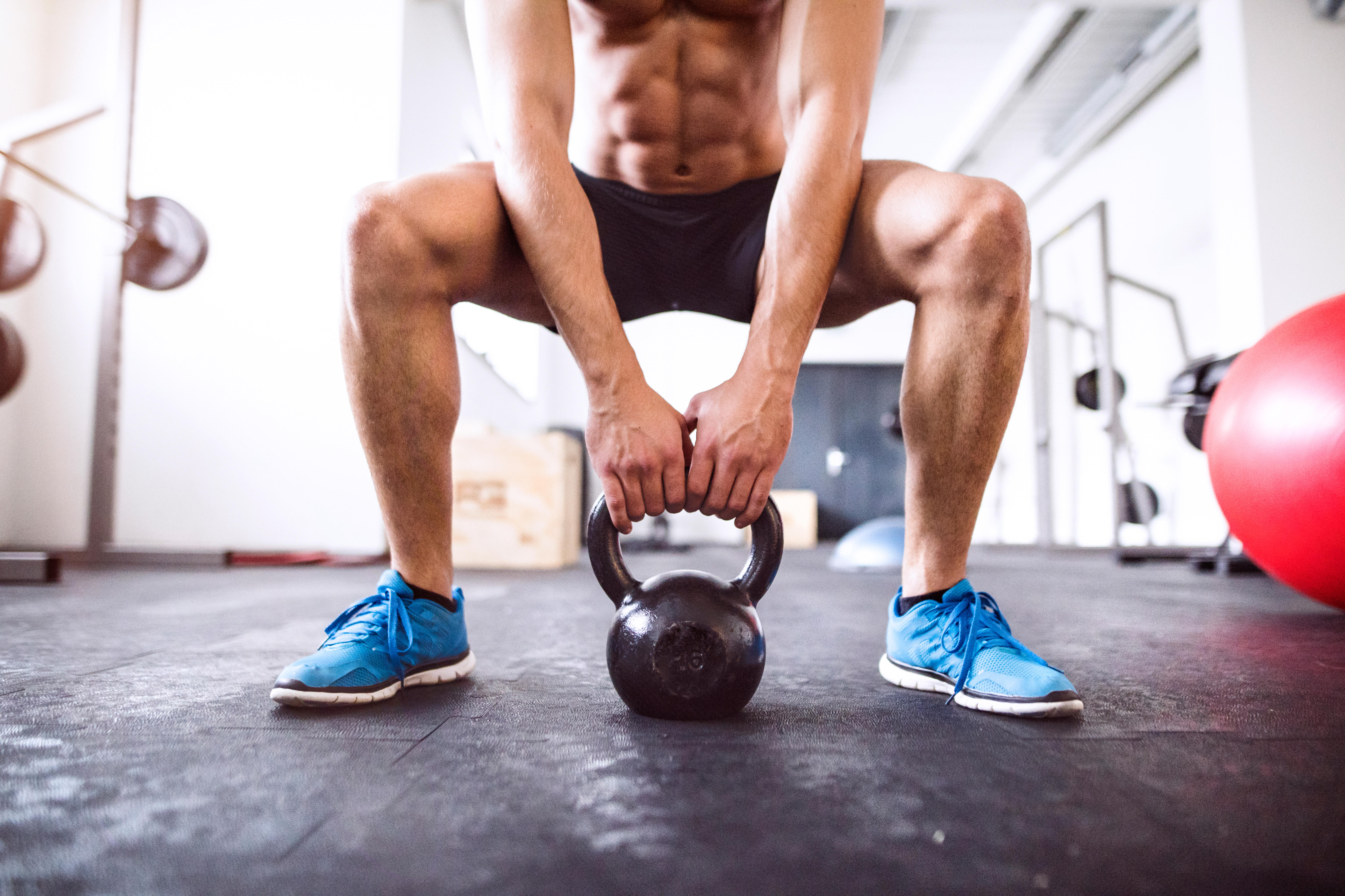 Man doing squats with a kettlebell in a gym