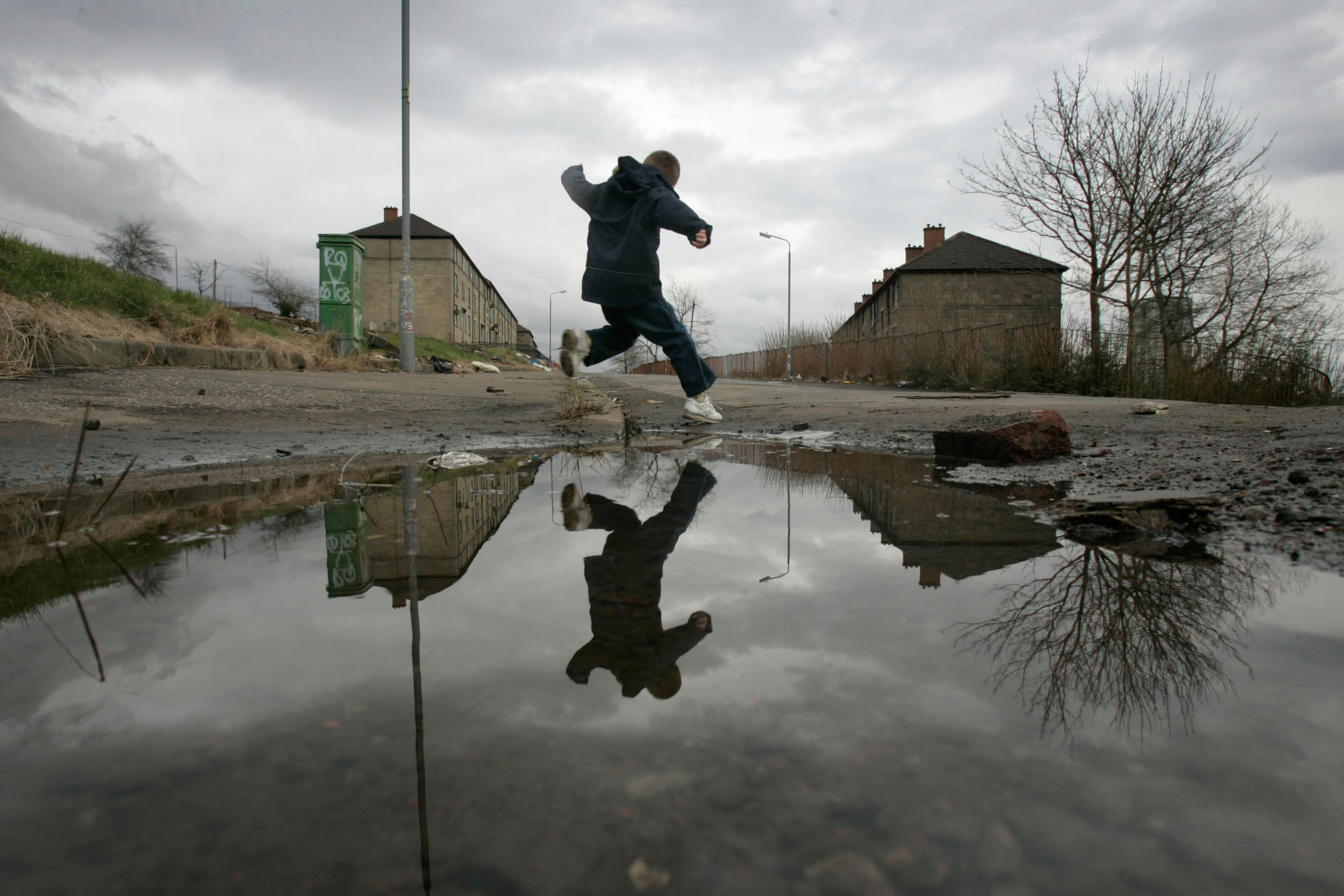 A child leaps over a puddle on a poverty stricken estate in Maryhill Glasgow