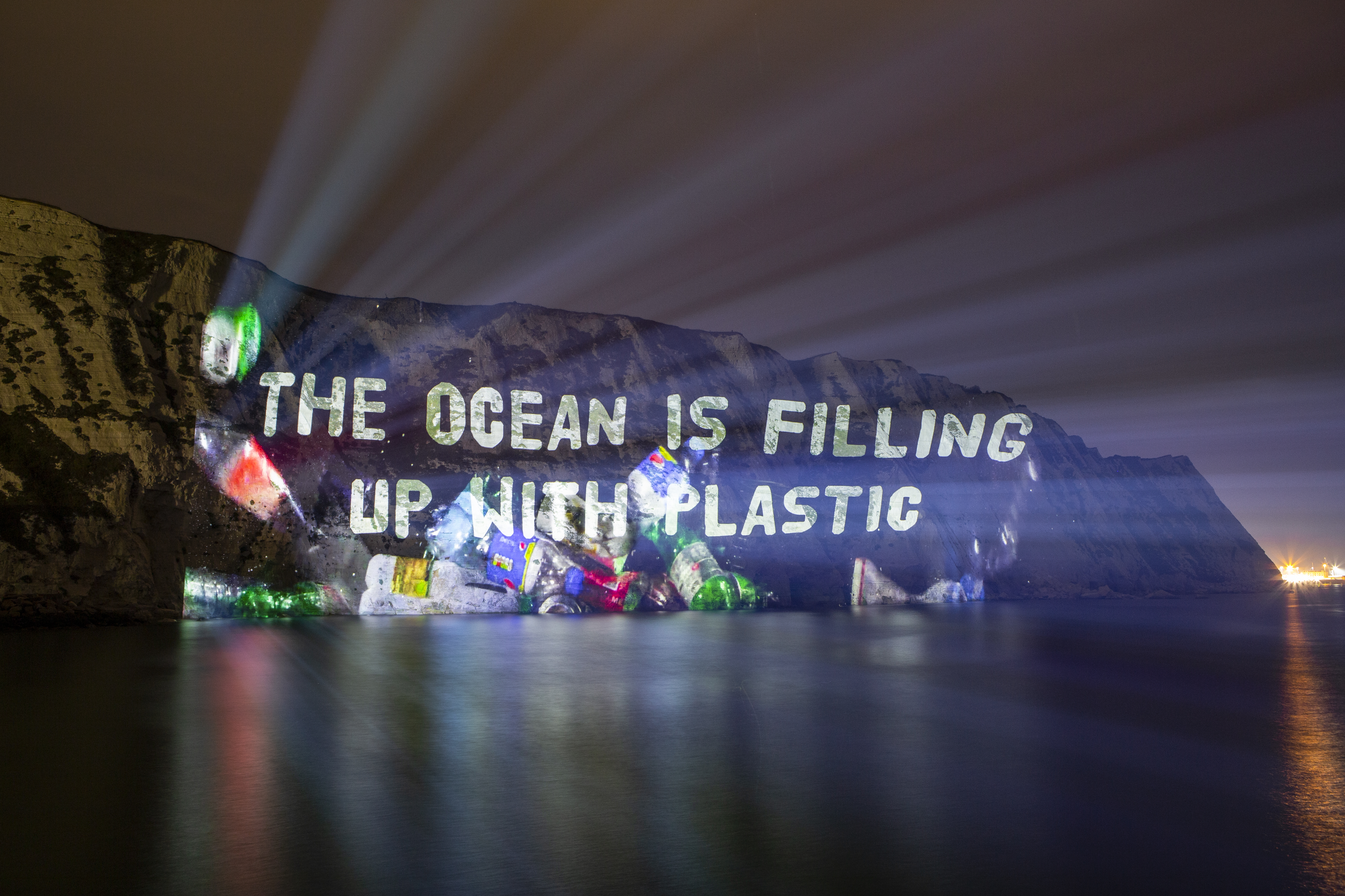 An image of litter and message saying the ocean is filling up with plastic projected onto the White Cliffs of Dover