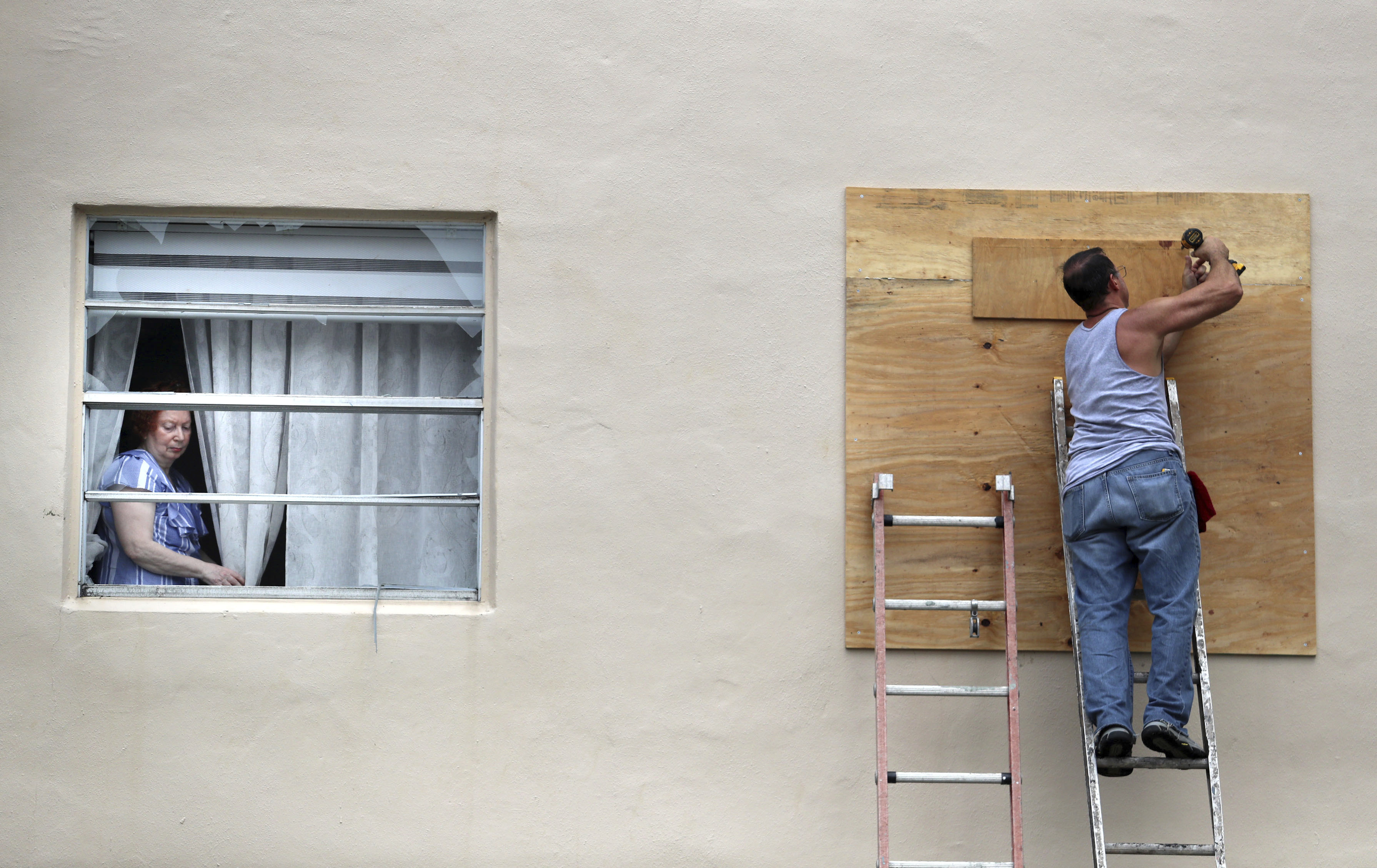 A King Point resident looks through her broken window as a man boards up another broken window from an apparent overnight tornado spawned from Hurricane Ian at Kings Point 55+ community in Delray Beach, Florida