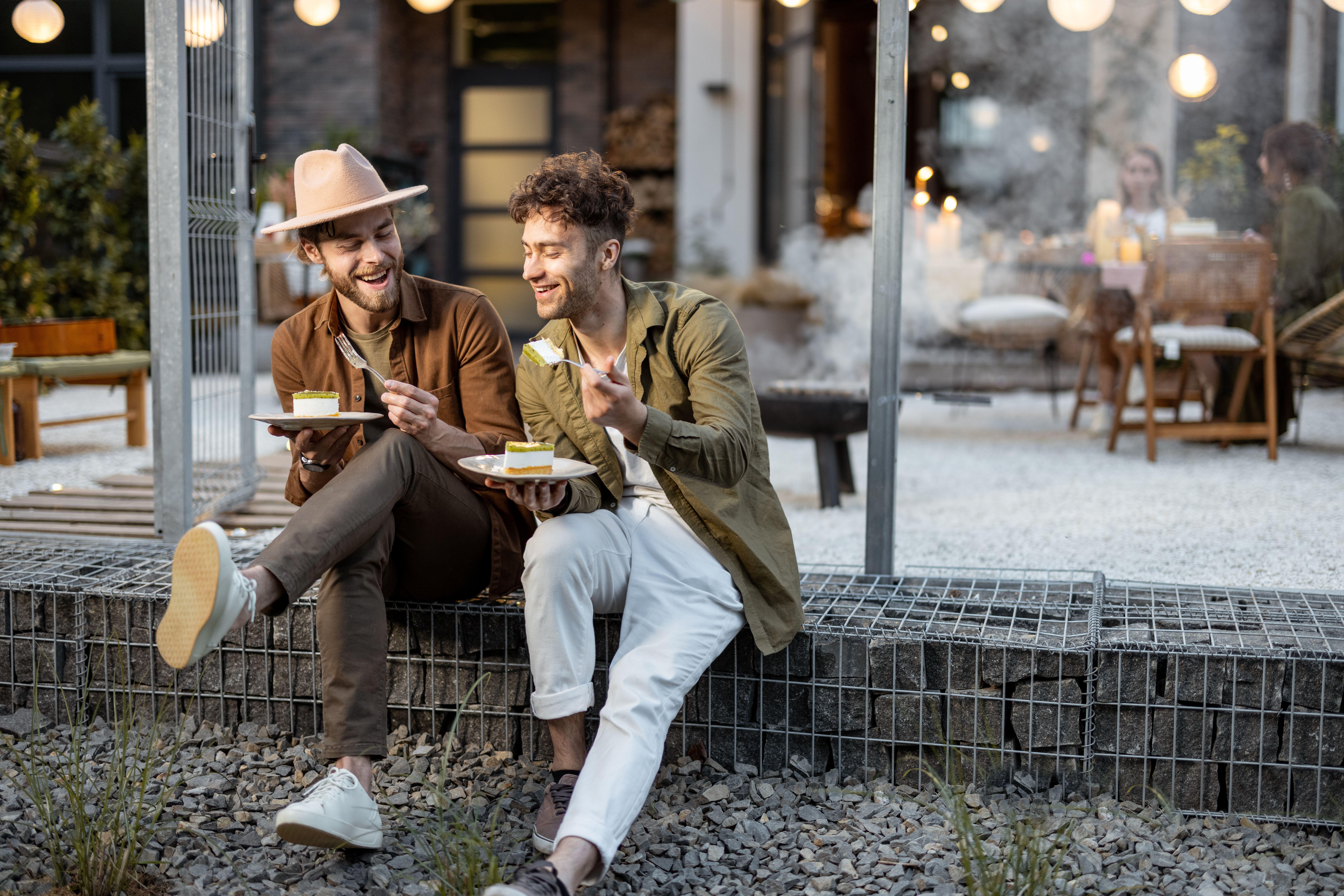 Two male friends chatting and eating cake outdoors
