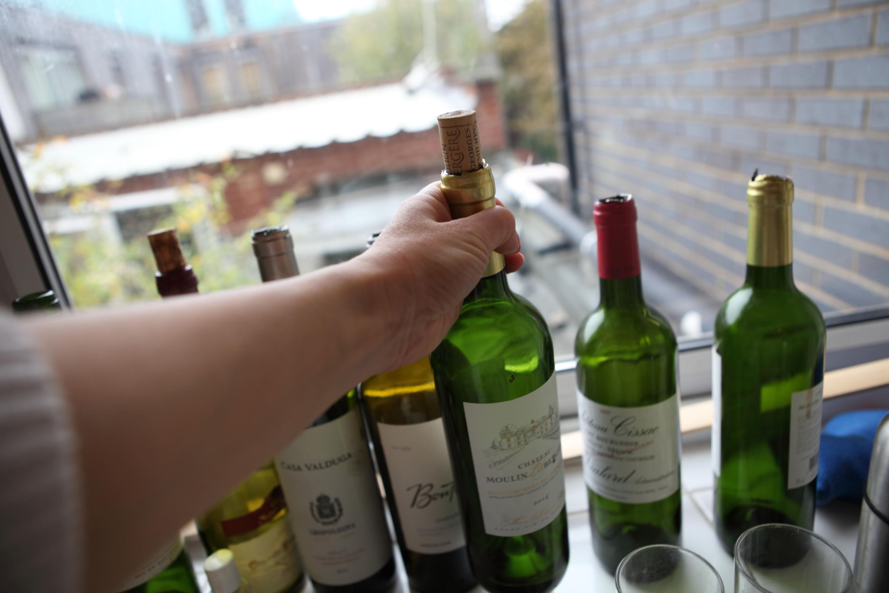 A hand places an empty wine bottle with the row of other empty wine bottles