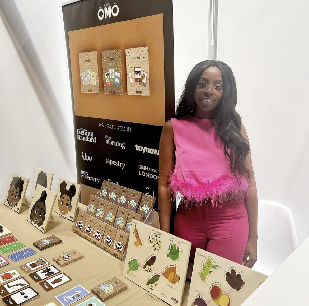 Woman smiling at the camera and standing next to a table with products on it