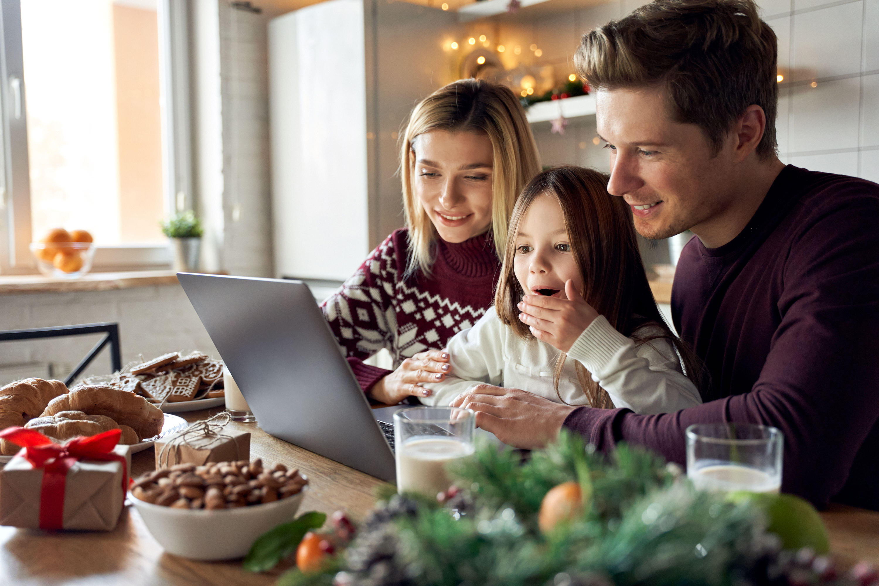 parents with excited kid daughter using laptop sitting at Christmas table