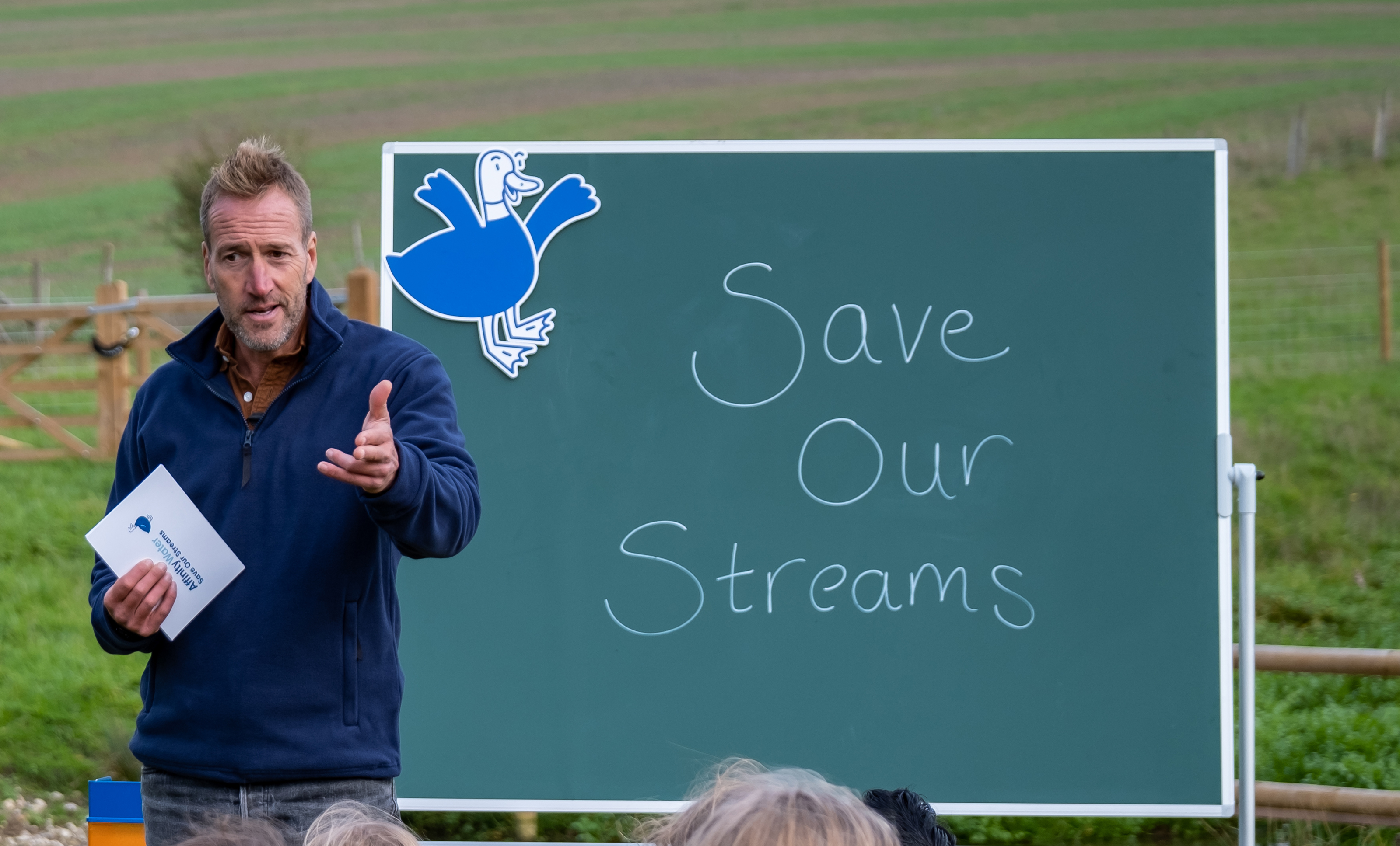Ben Fogle standing near a chalkboard reading 'Save our Streams'