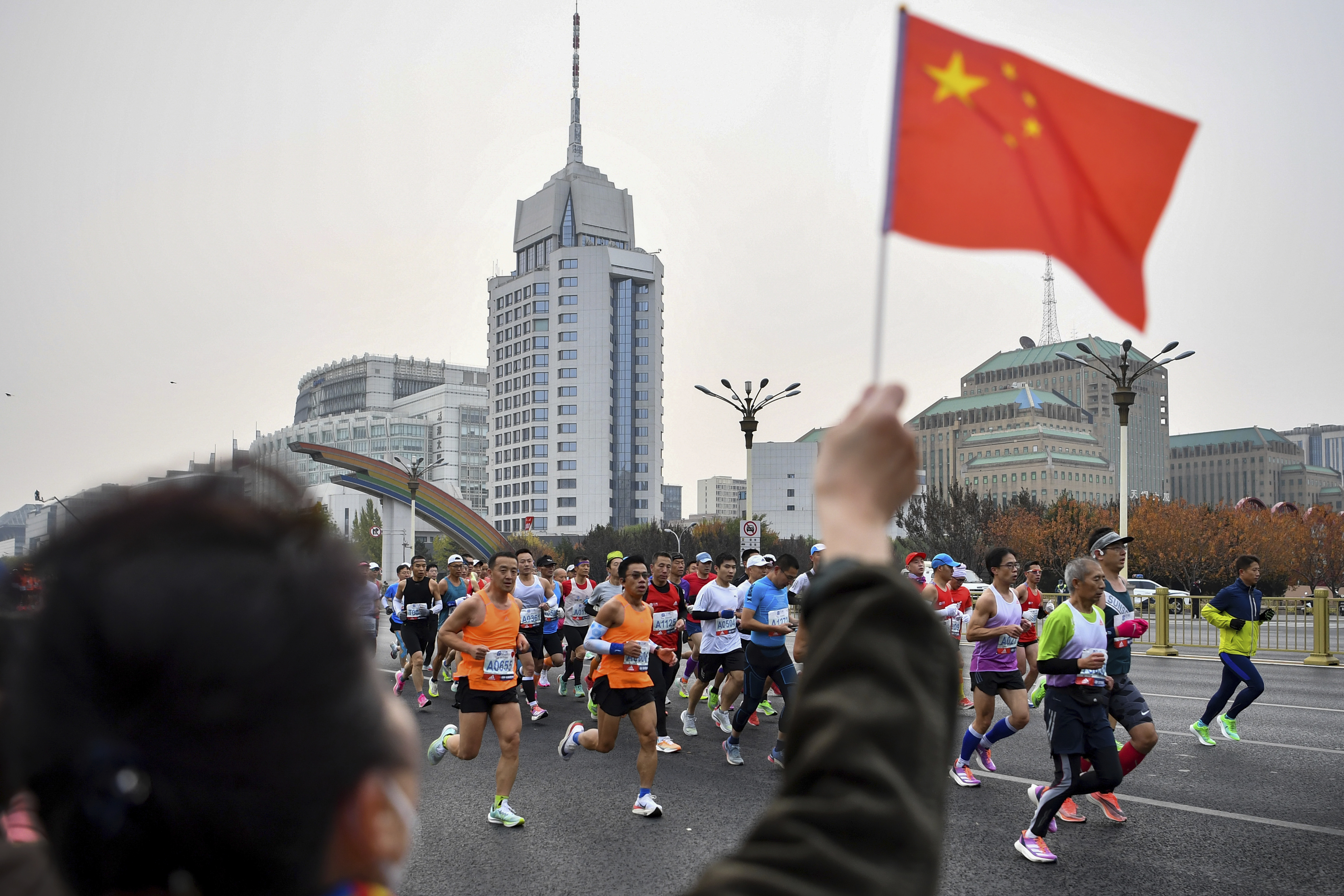 A spectator waves a national flag as runners compete in the Beijing Marathon