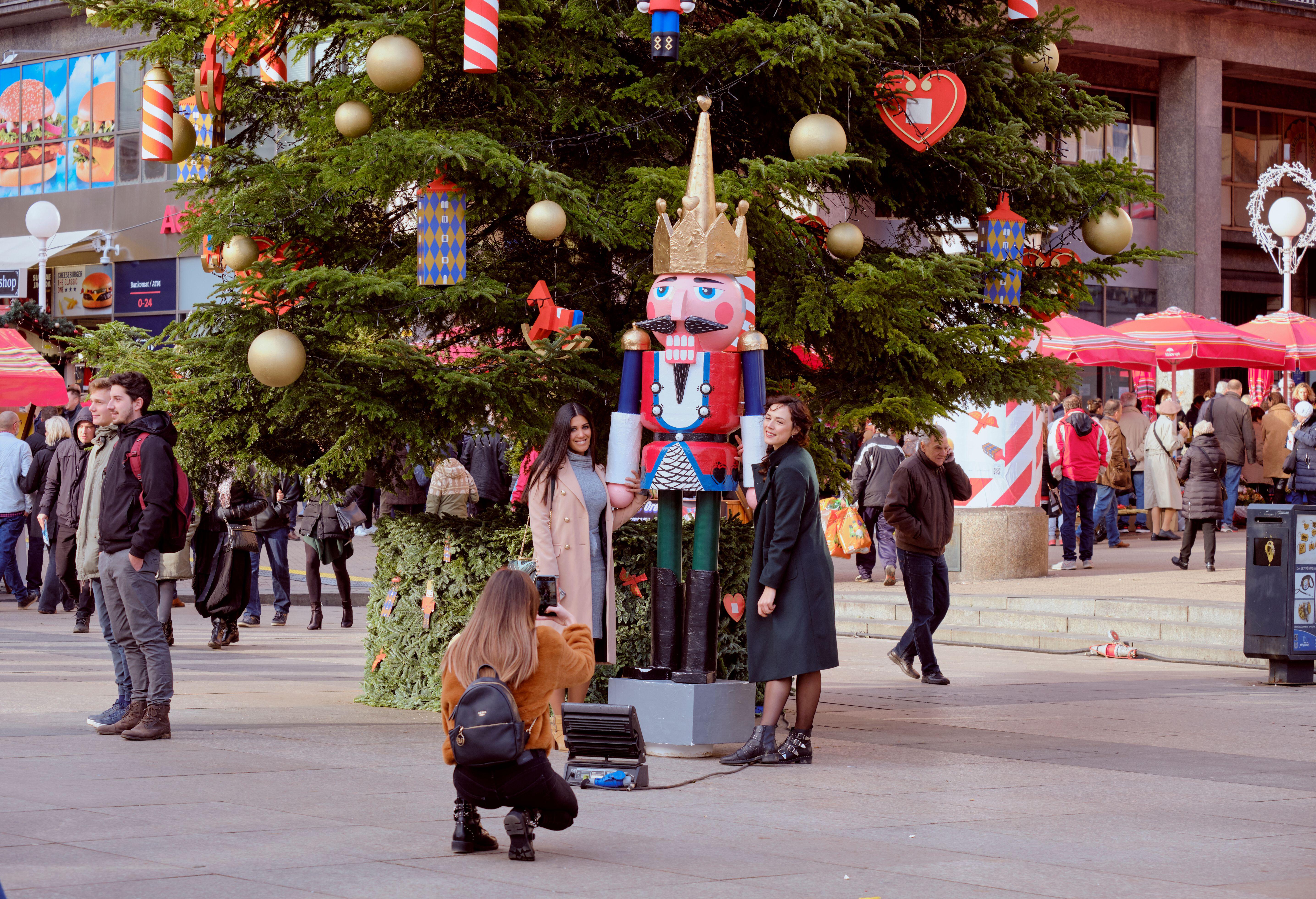 Two women posing next to one of the Nutcracker statue next to large Christmas tree in centre square at Advent Market. Zagreb, Croatia