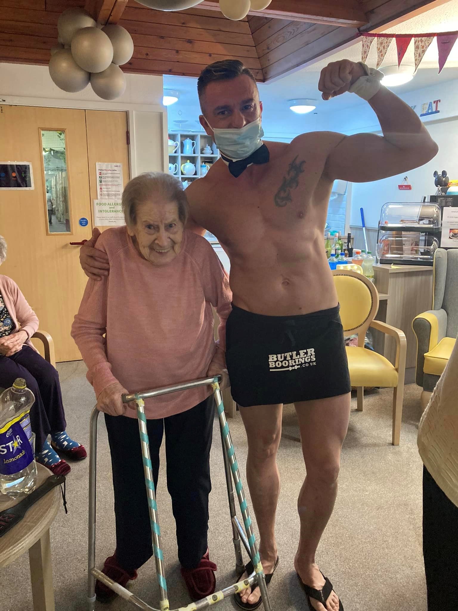 Man flexing his arm muscle and posing with a woman holding onto a zimmer frame