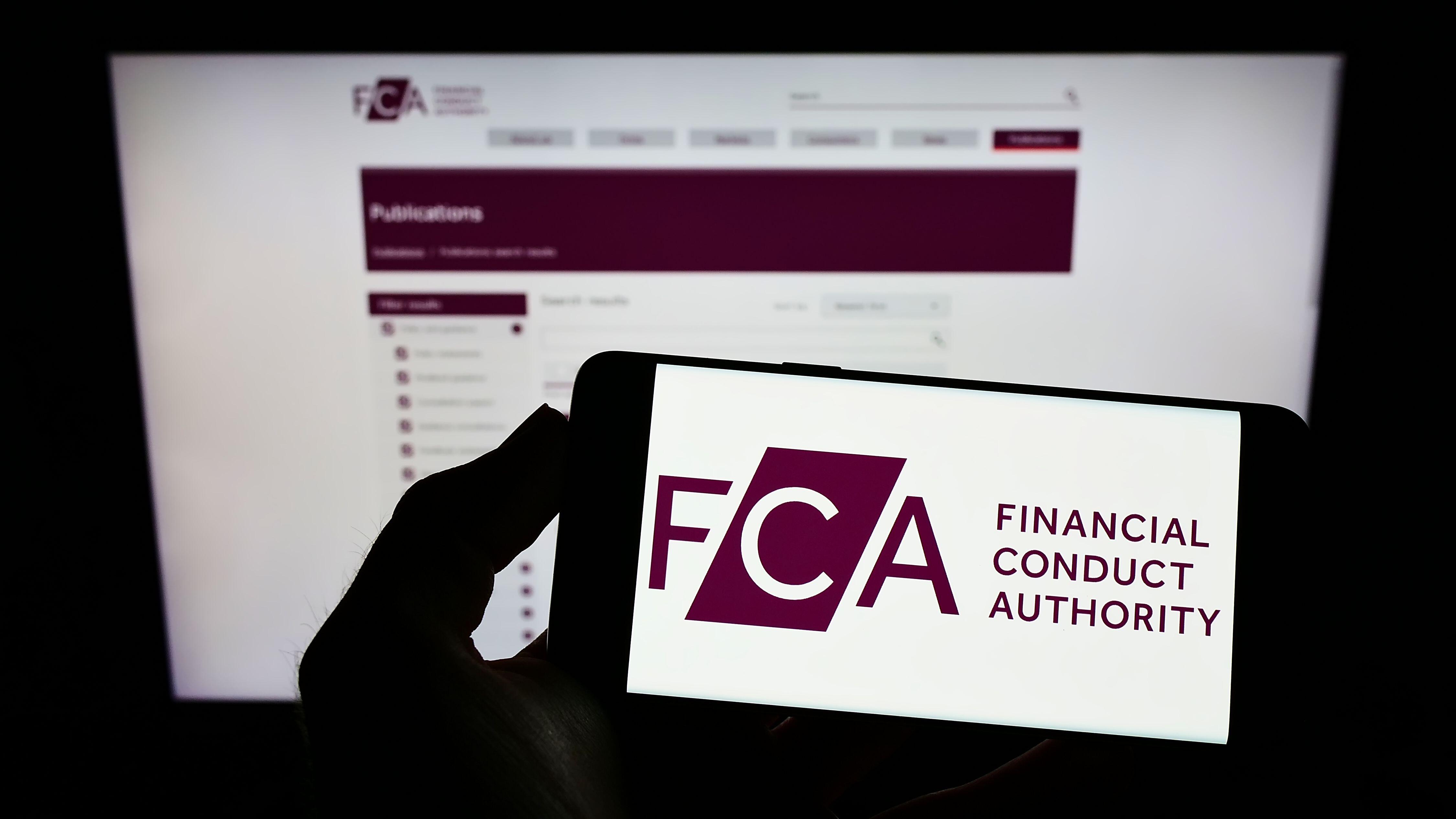 Person holding mobile phone with logo of the Financial Conduct Authority on screen in front of webpage