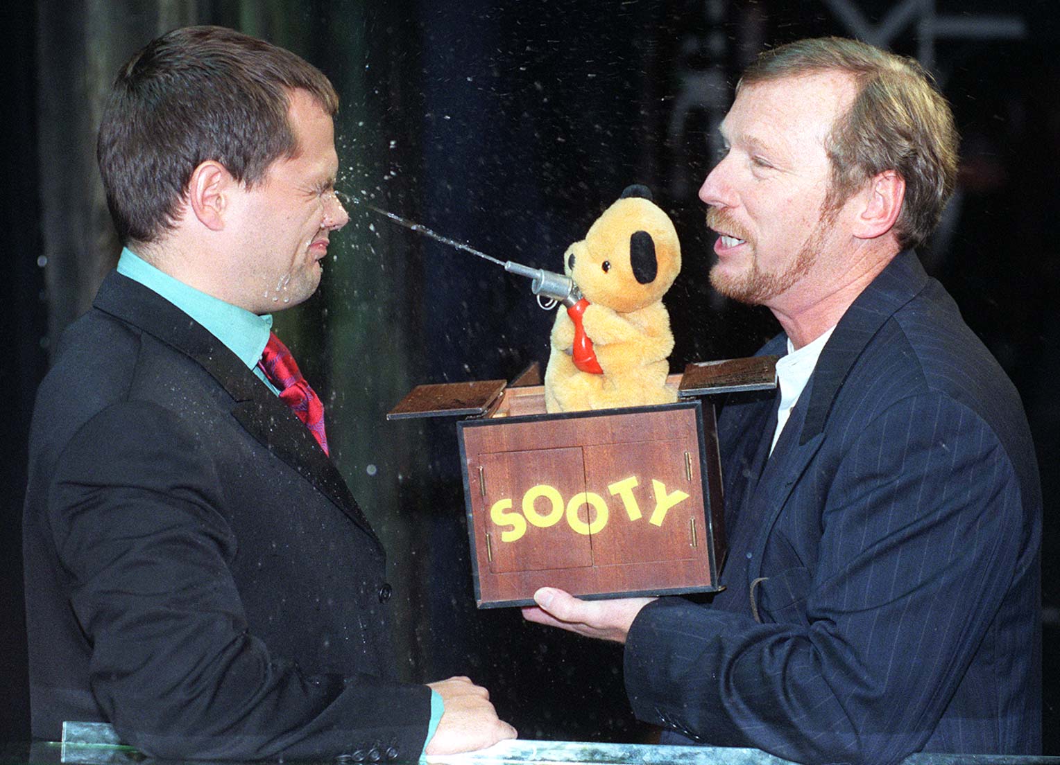 Comedian Jack Dee is squirted in the face by Sooty and puppeteer Matthew Corbett