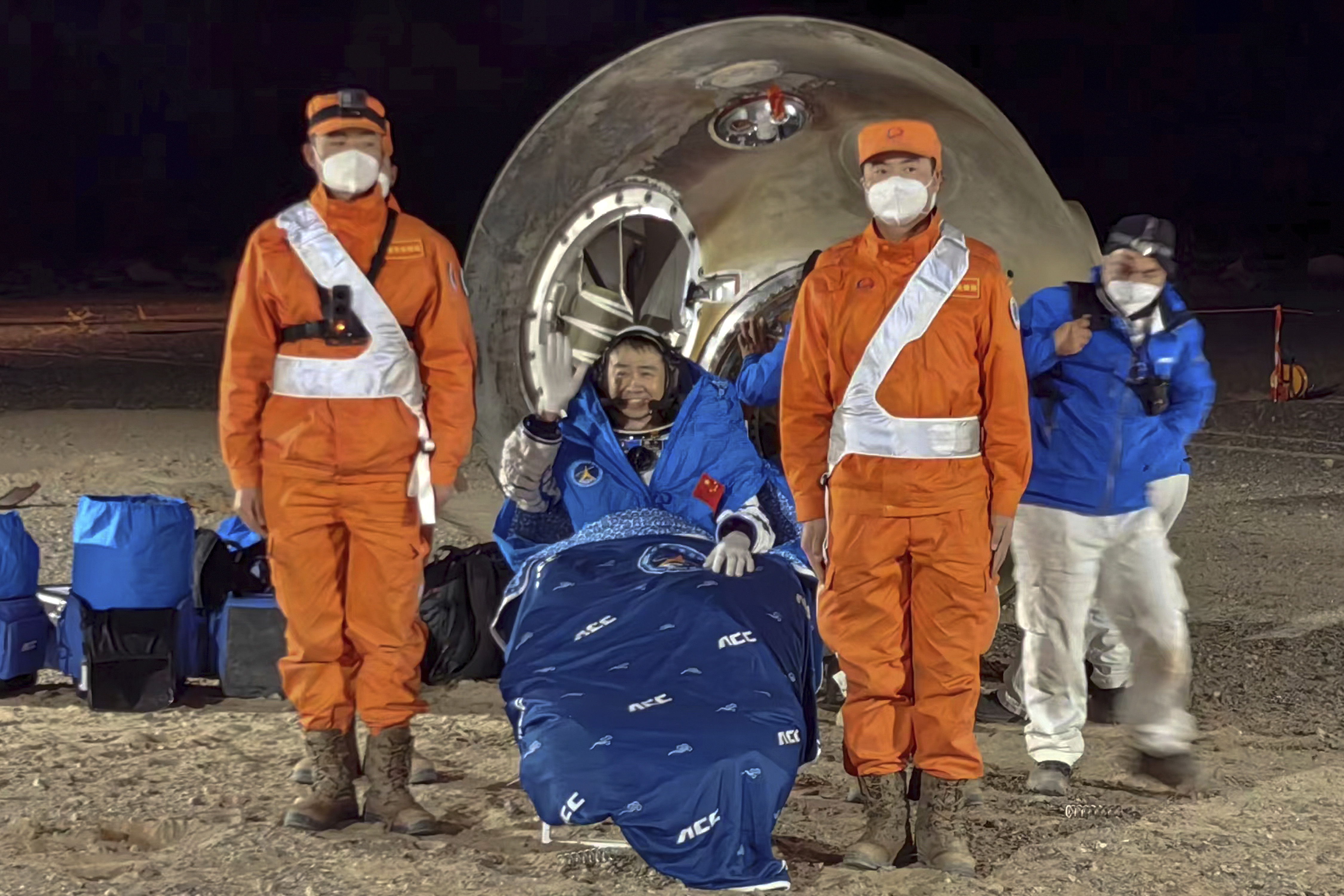 Astronaut Chen Dong waves as he sits outside the re-entry capsule 