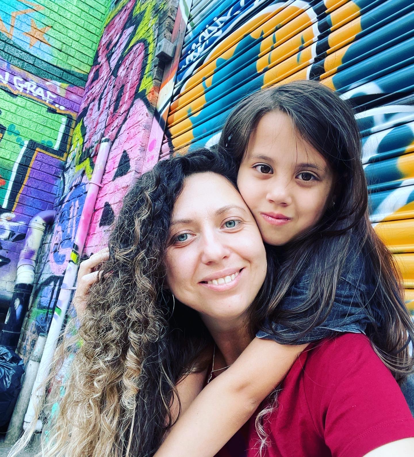 Little girl with her arm over a woman's shoulder, with both looking at the camera