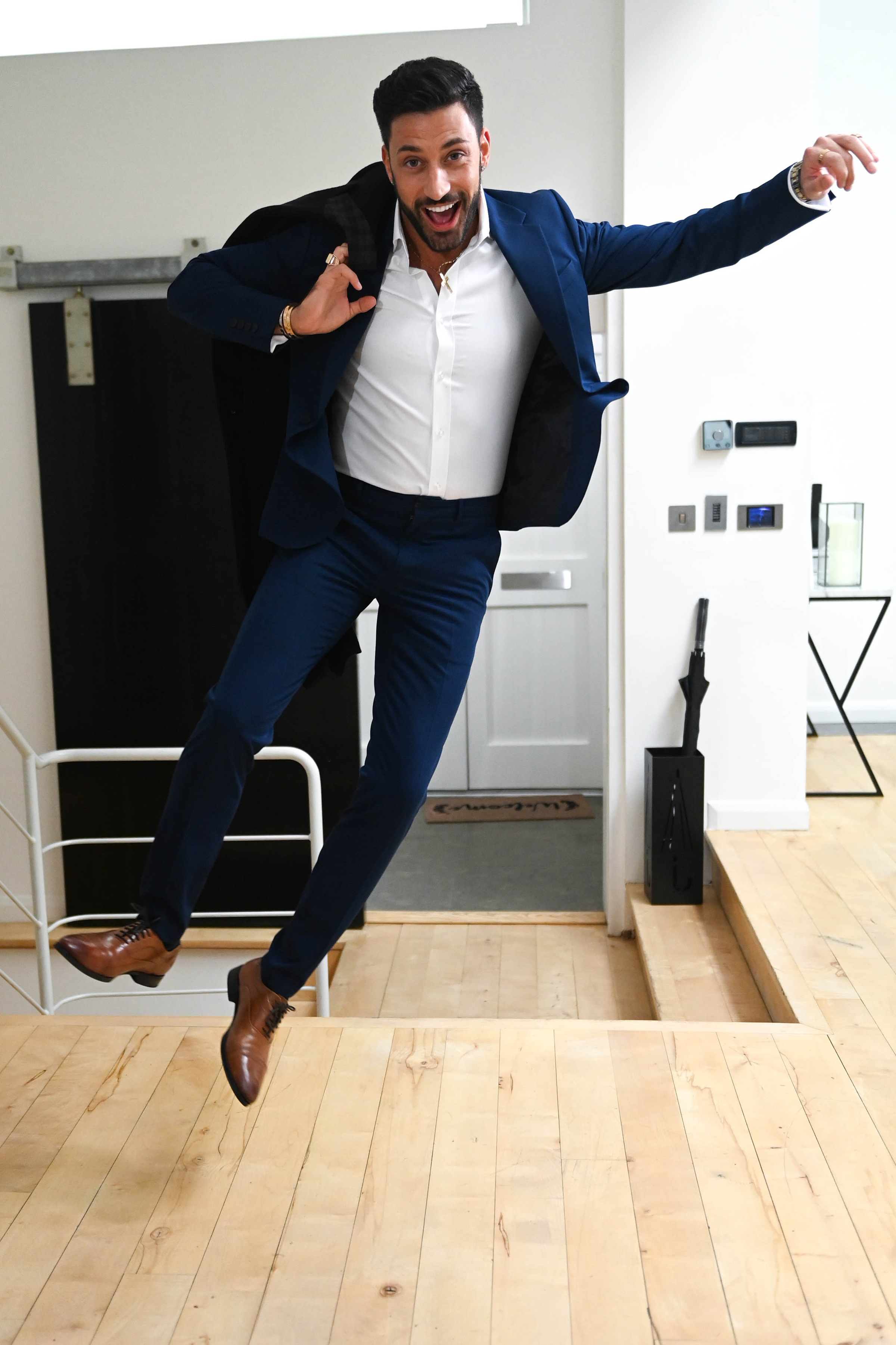 Giovanni Pernice jumping in the air, doing a heel click, wearing a dapper dark blue suit