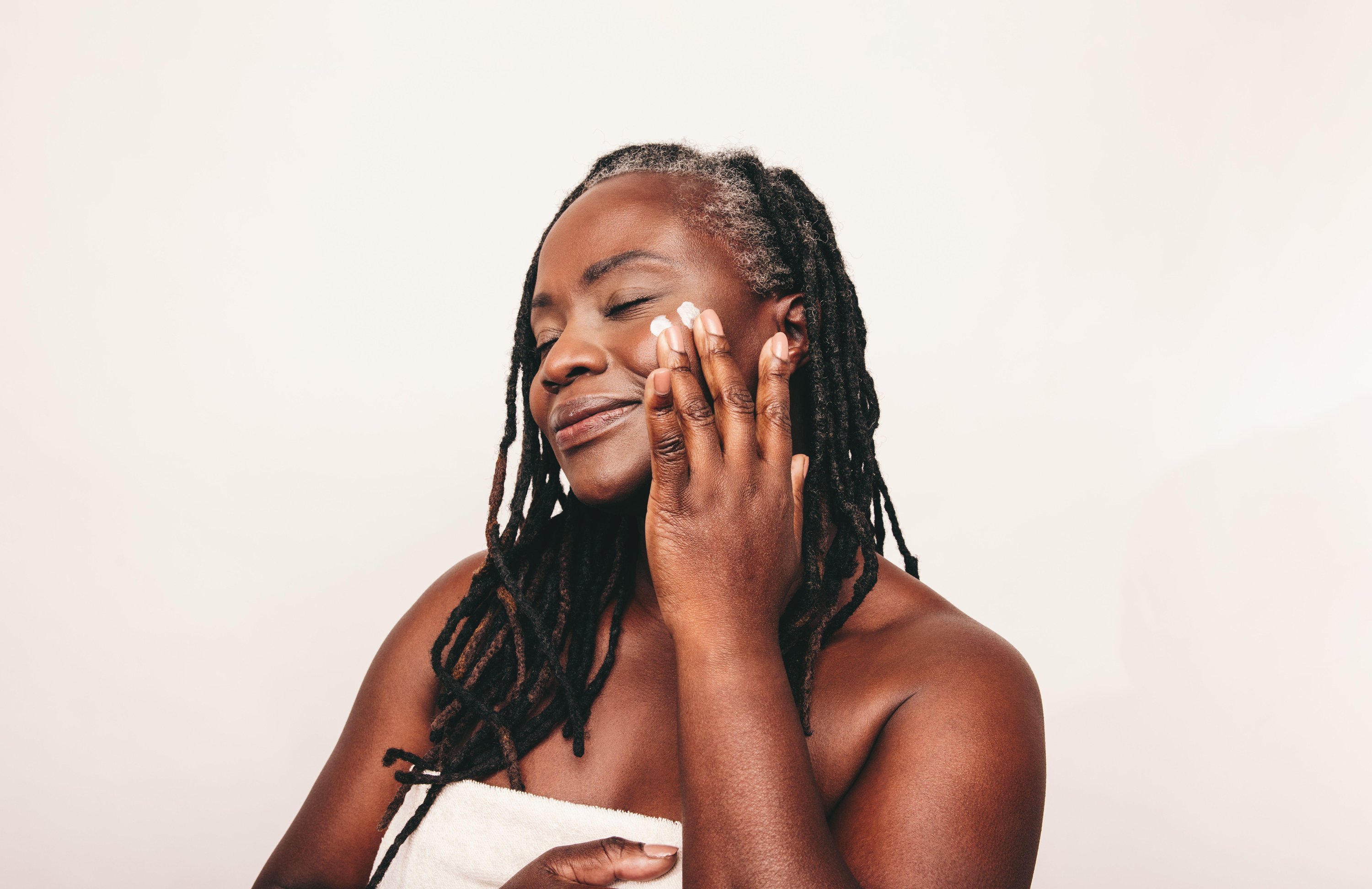 woman with dreadlocks applying moisturising cream on her face