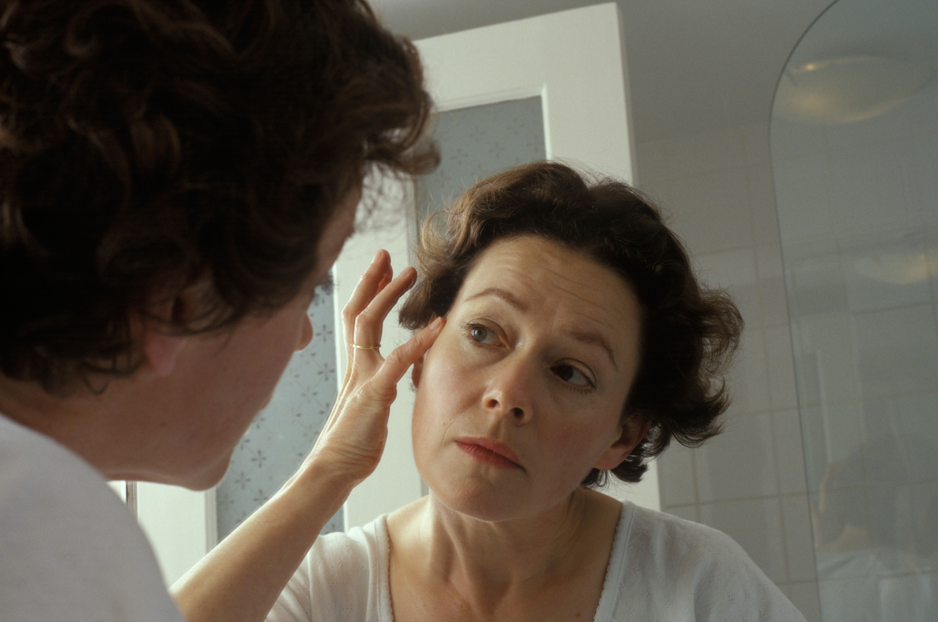 woman looking at her wrinkles in the mirror