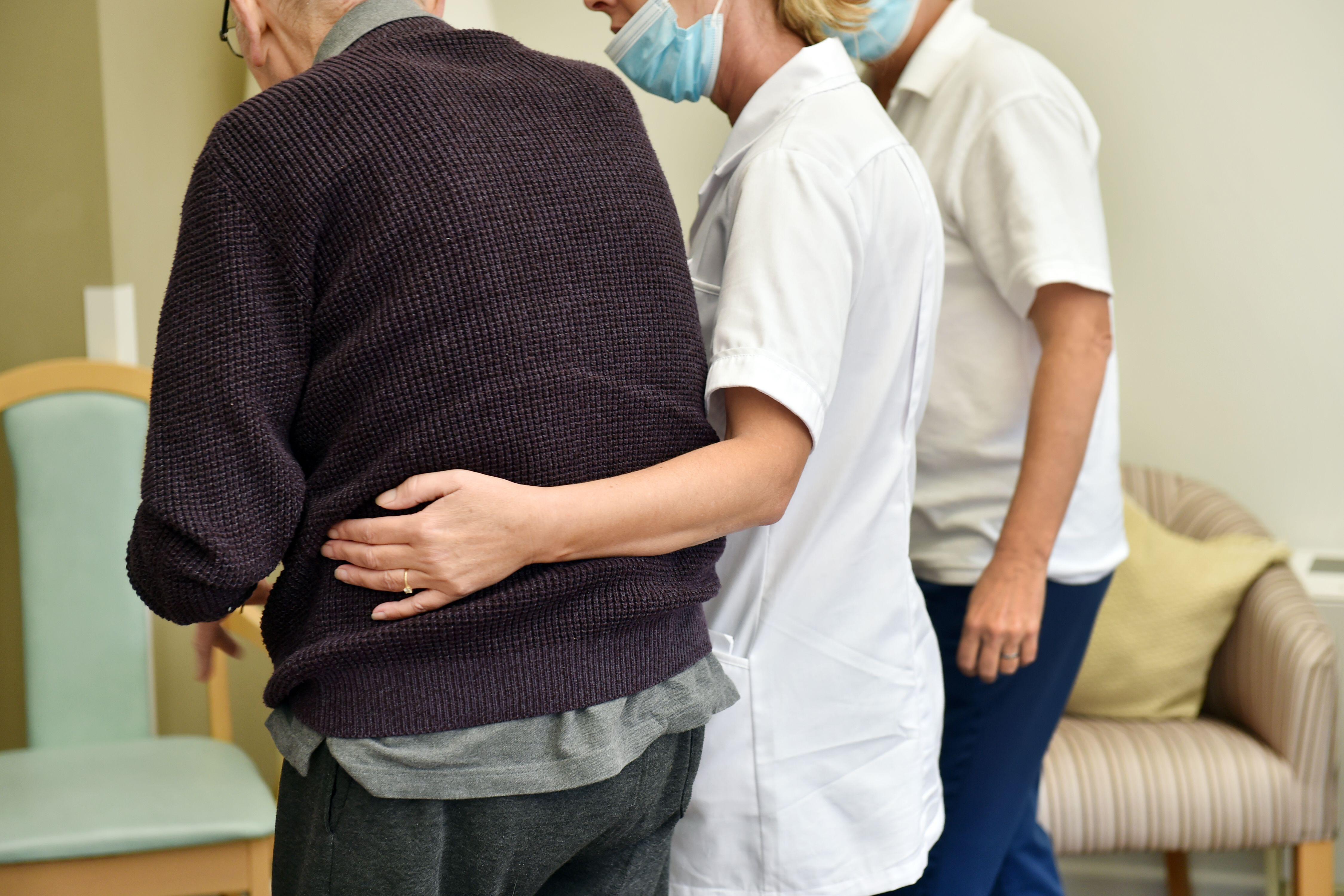 Care home staff help elderly people move about the care home