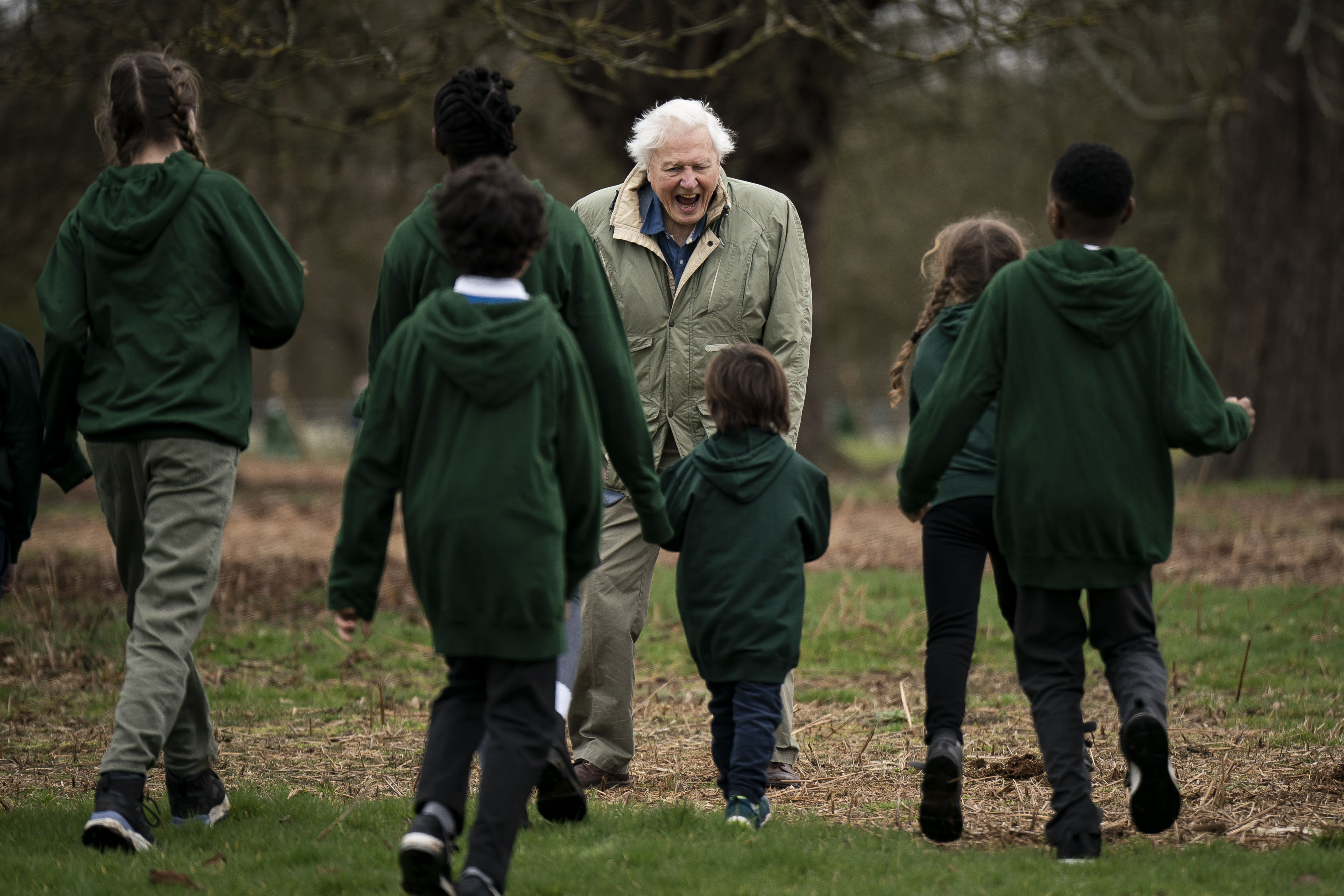 Sir David Attenborough  with schoolchildren as he plants the tree in Richmond Park