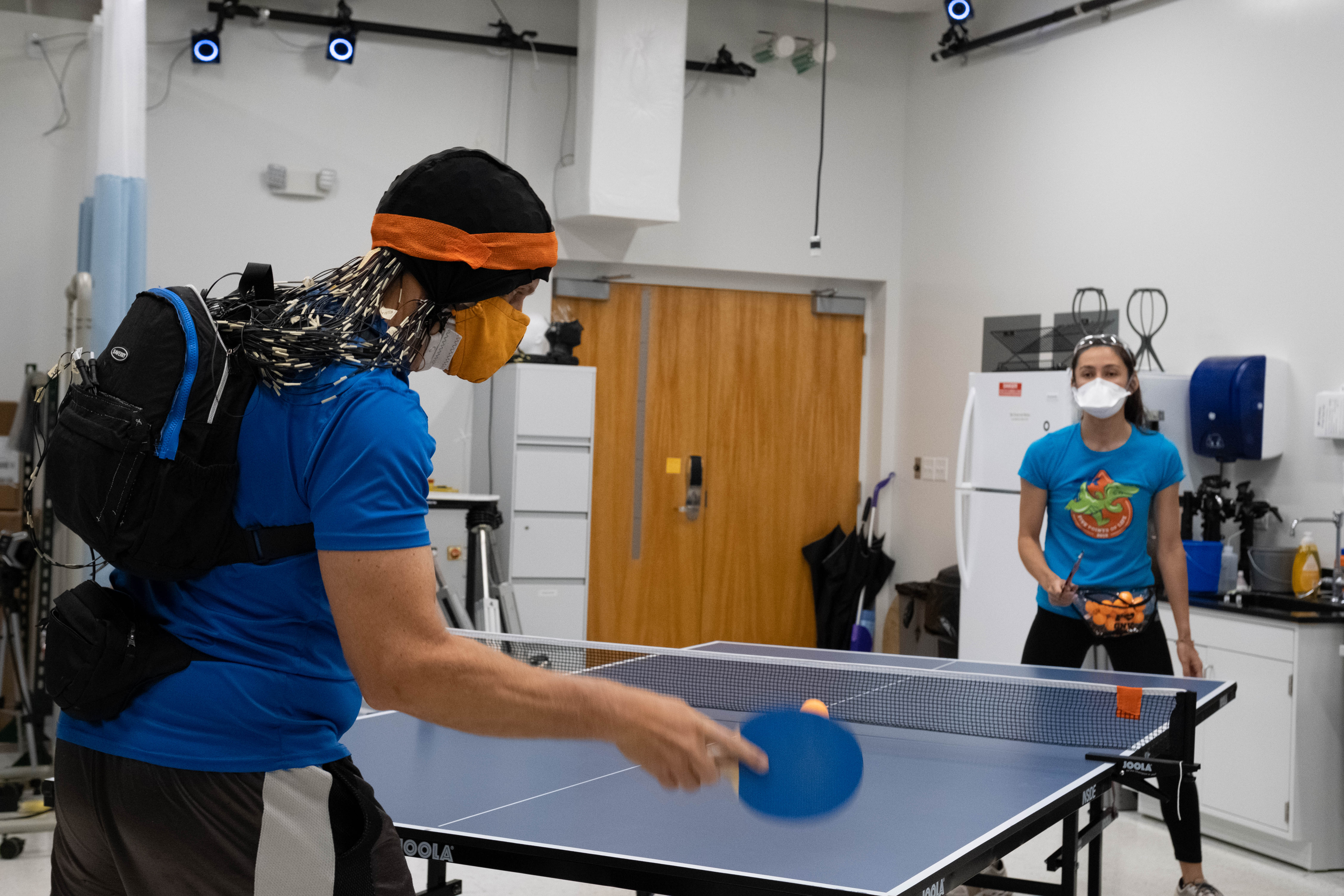 A participant plays table tennis against graduate student Amanda Studnicki while having his brain imaged via an EEG cap