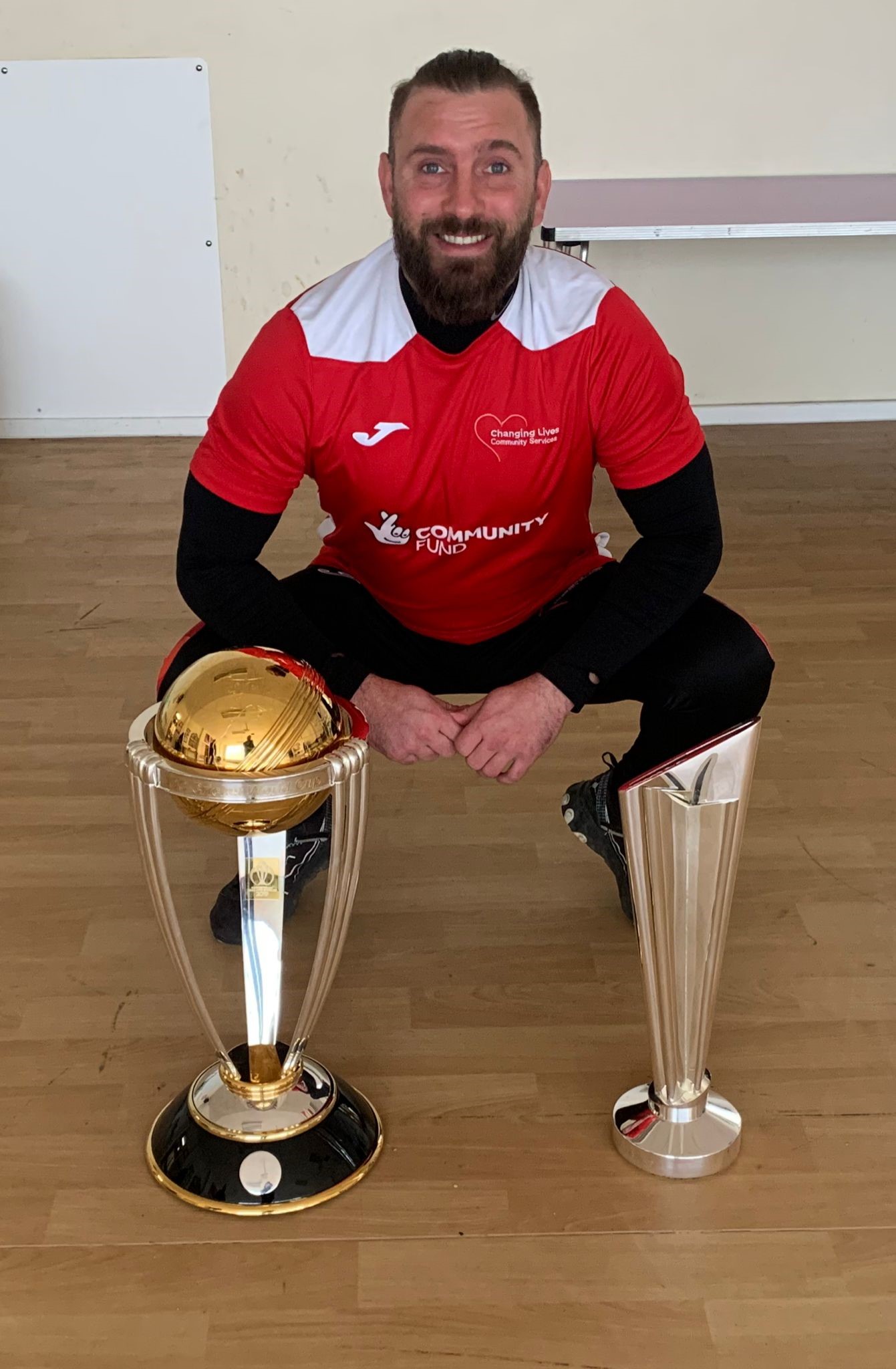 Man kneeling down, with two trophies near his feet 