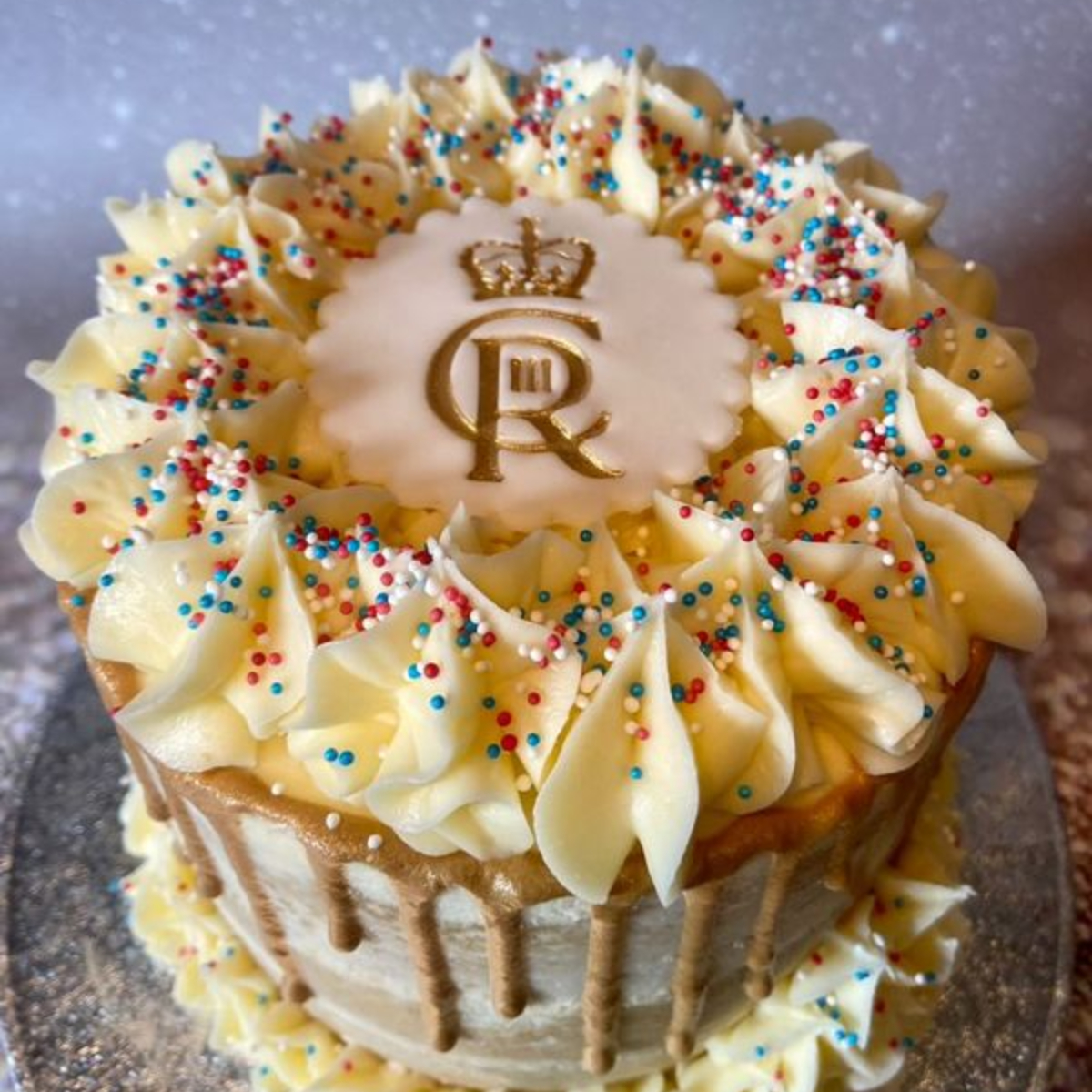 A vanilla sponge decorated with a gold royal insignia and gold drip down the sides