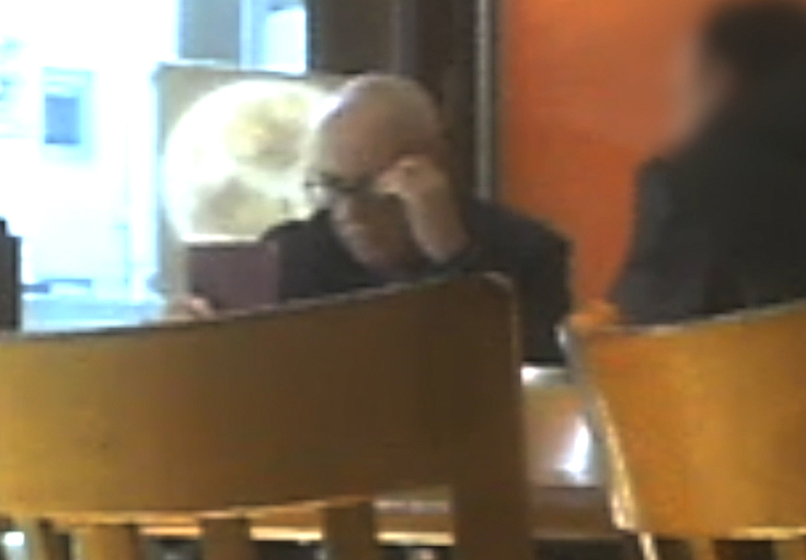 Anthony Beard sitting at a table in a cafe during a meeting with one of his clients, holding a passport.